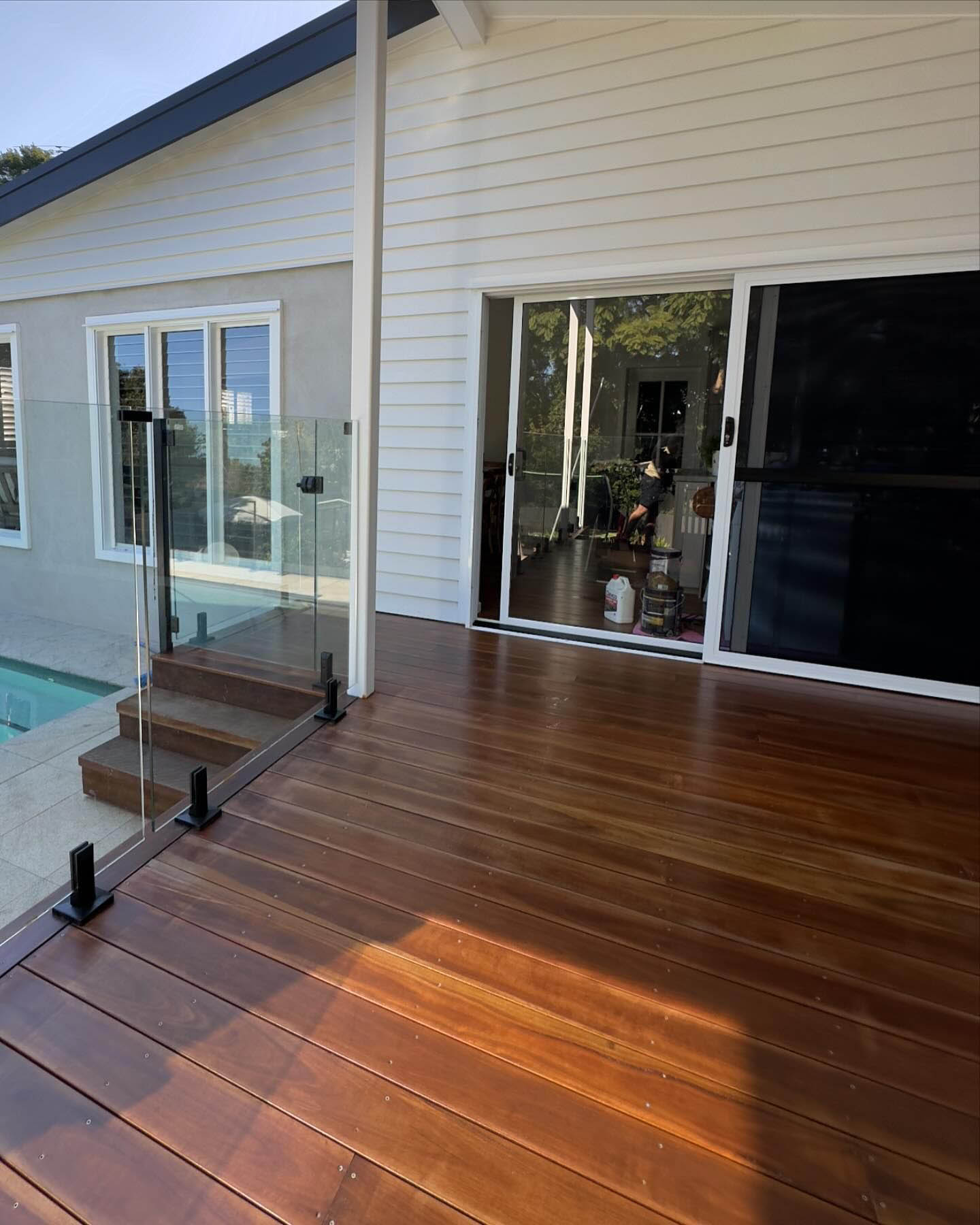 Oiled timber deck with glass pool fencing beside a white weatherboard house