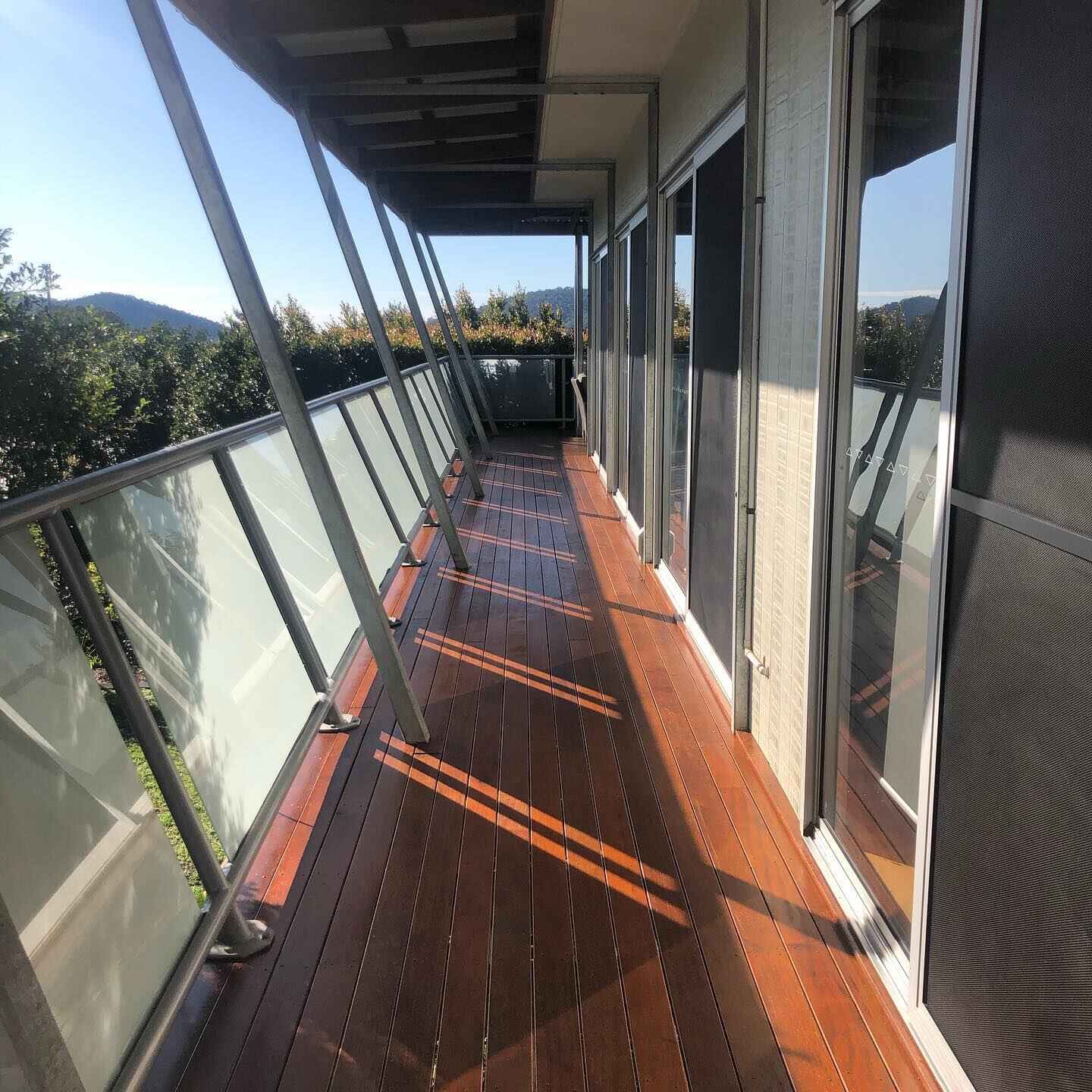 Narrow oiled timber balcony with glass balustrade and angled posts