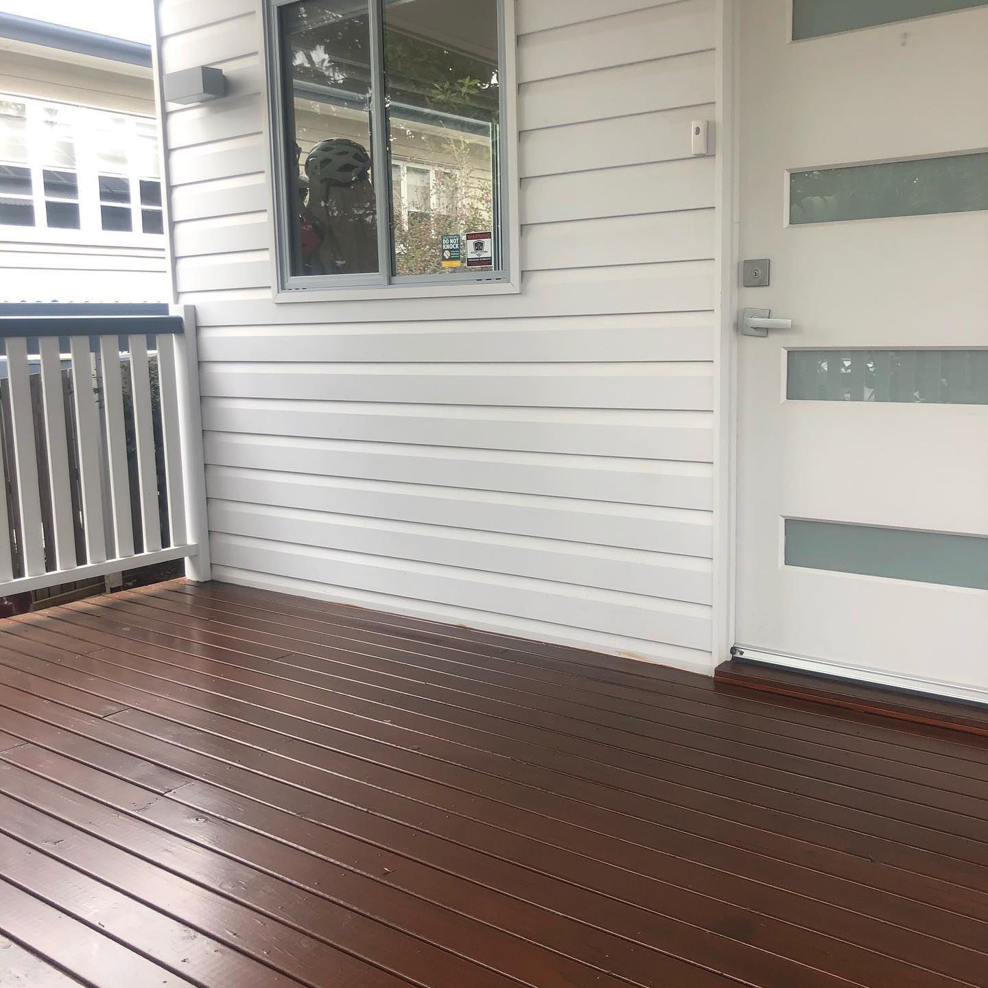 Dark oiled timber verandah at a white front door with white balustrade