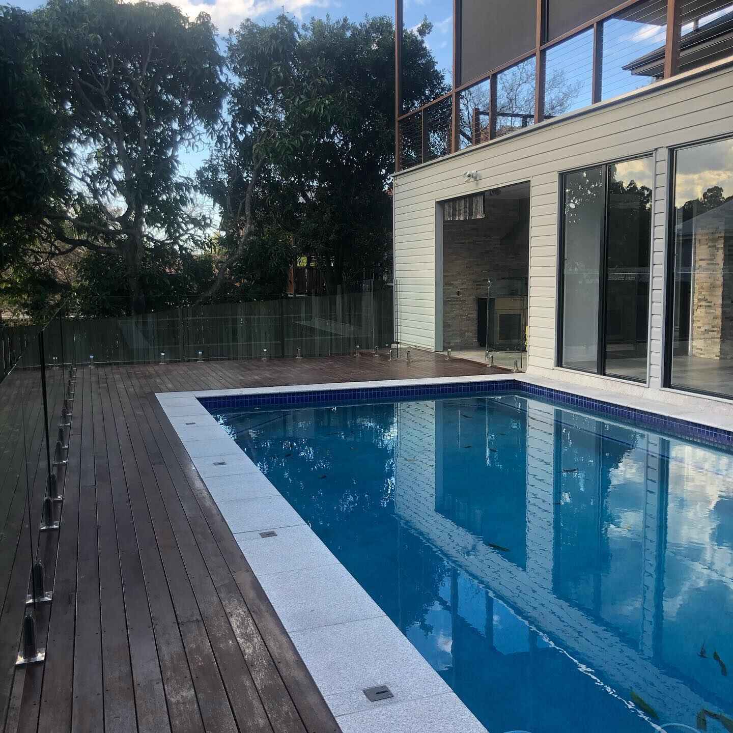 Dark oiled timber deck along a lap pool with glass fencing