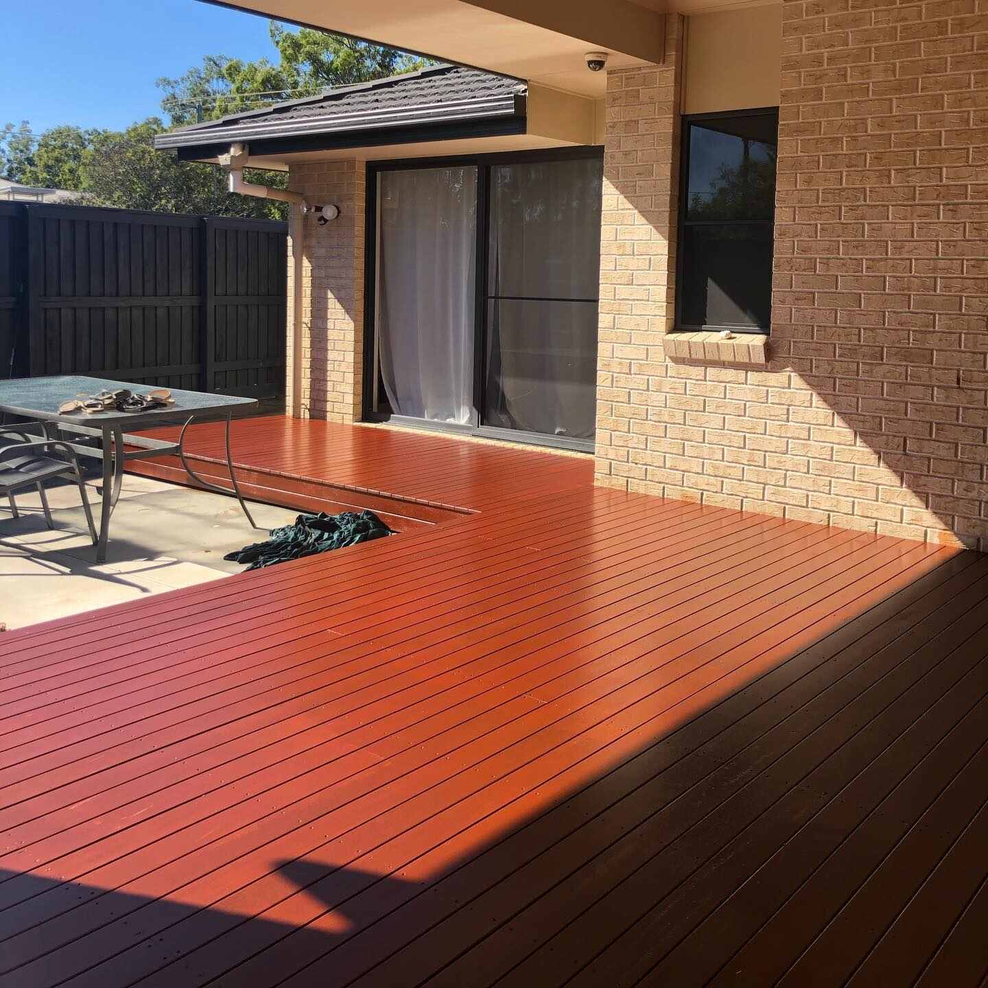 Freshly oiled red-toned deck beside a brick house in the sun