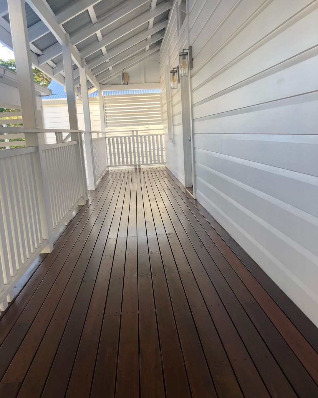 Narrow dark oiled timber verandah with white balustrade along weatherboards