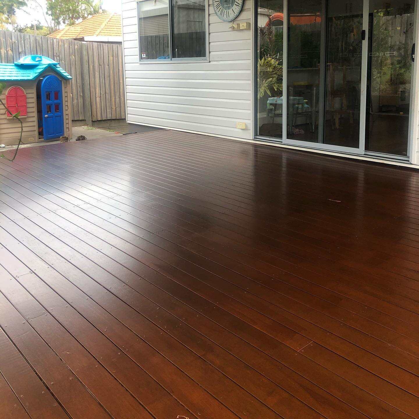 Glossy dark oiled timber deck beside a cubby house and sliding doors