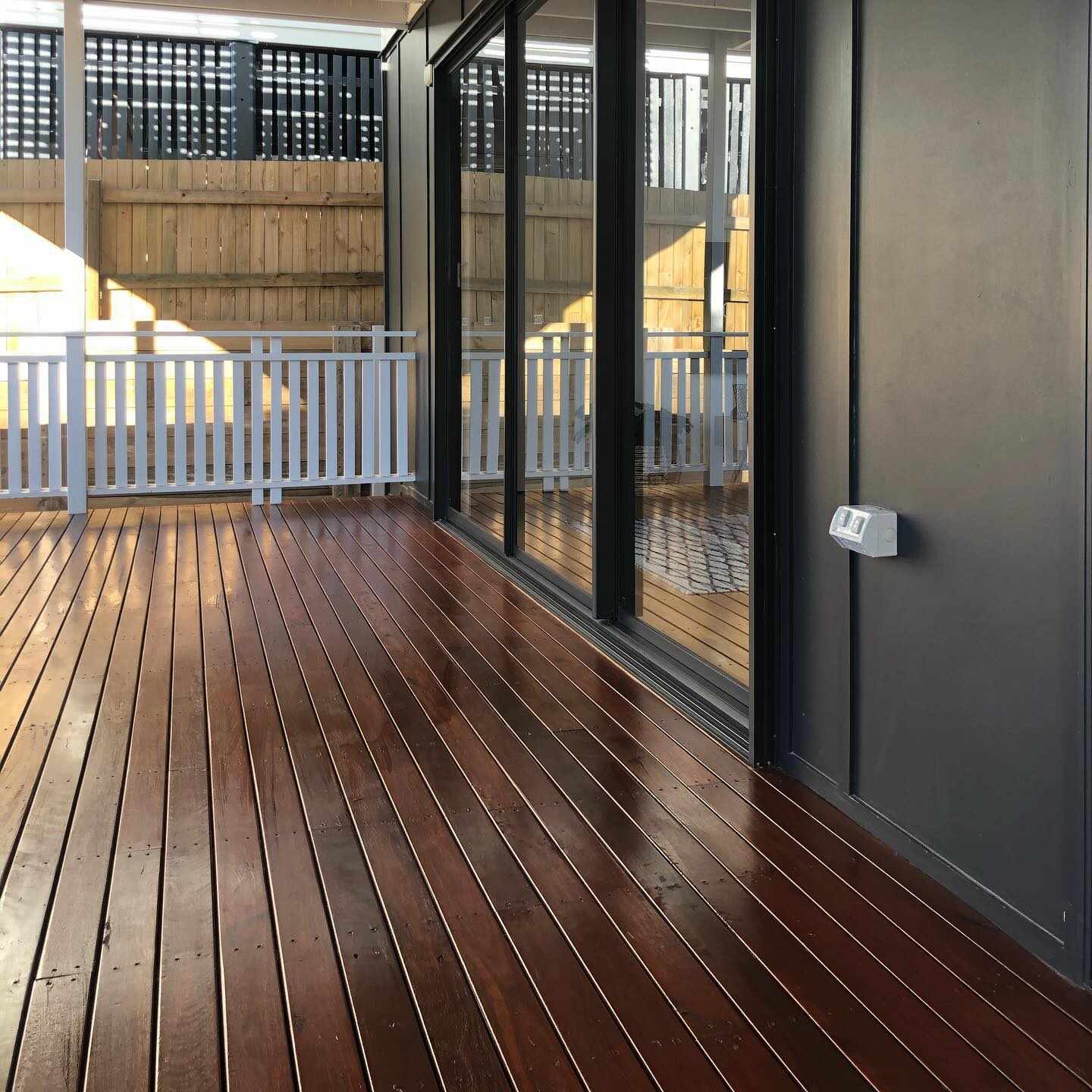 Glossy oiled timber deck beside black-framed glass doors and white balustrade