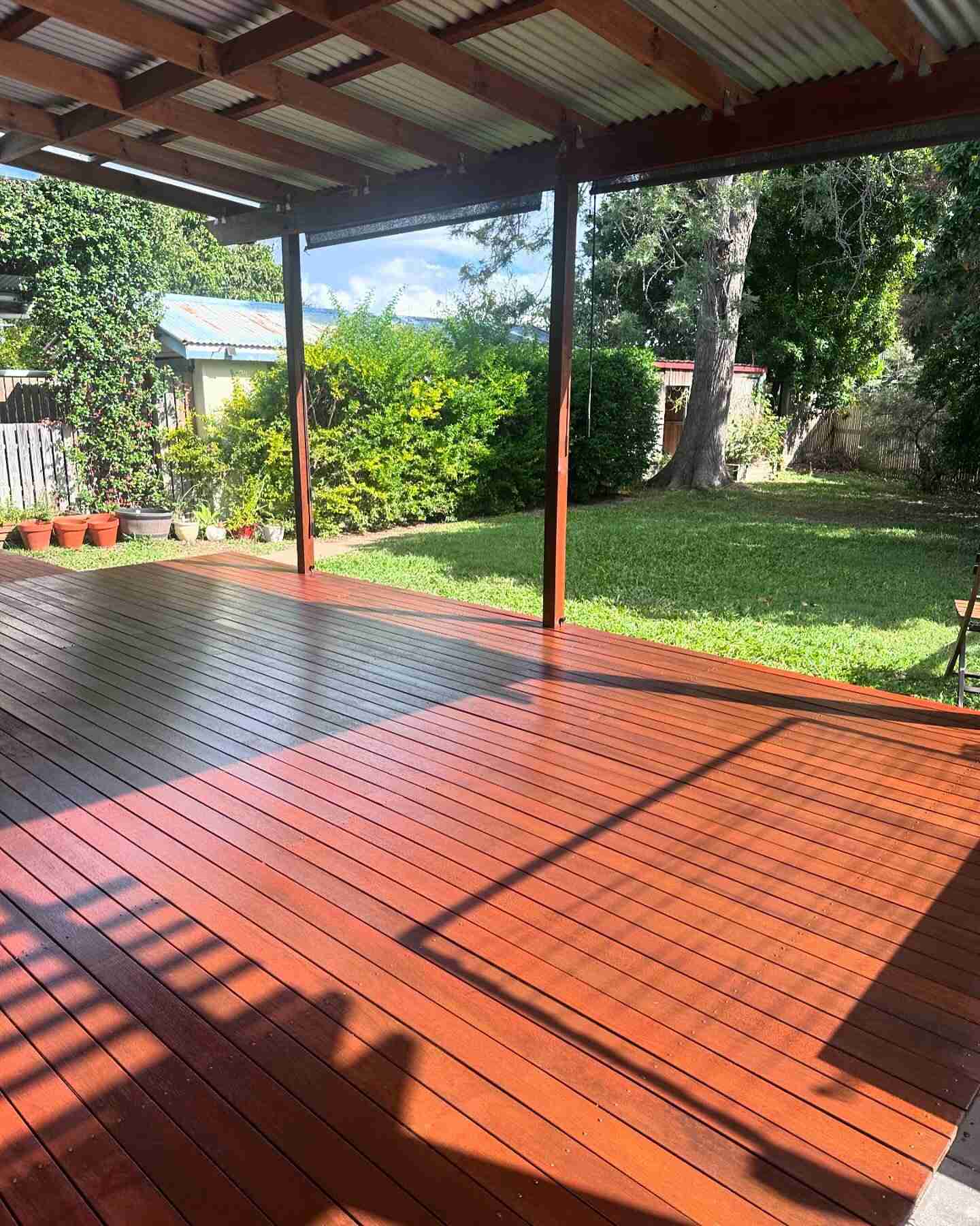 Oiled timber deck under a timber-framed patio roof overlooking a lawn