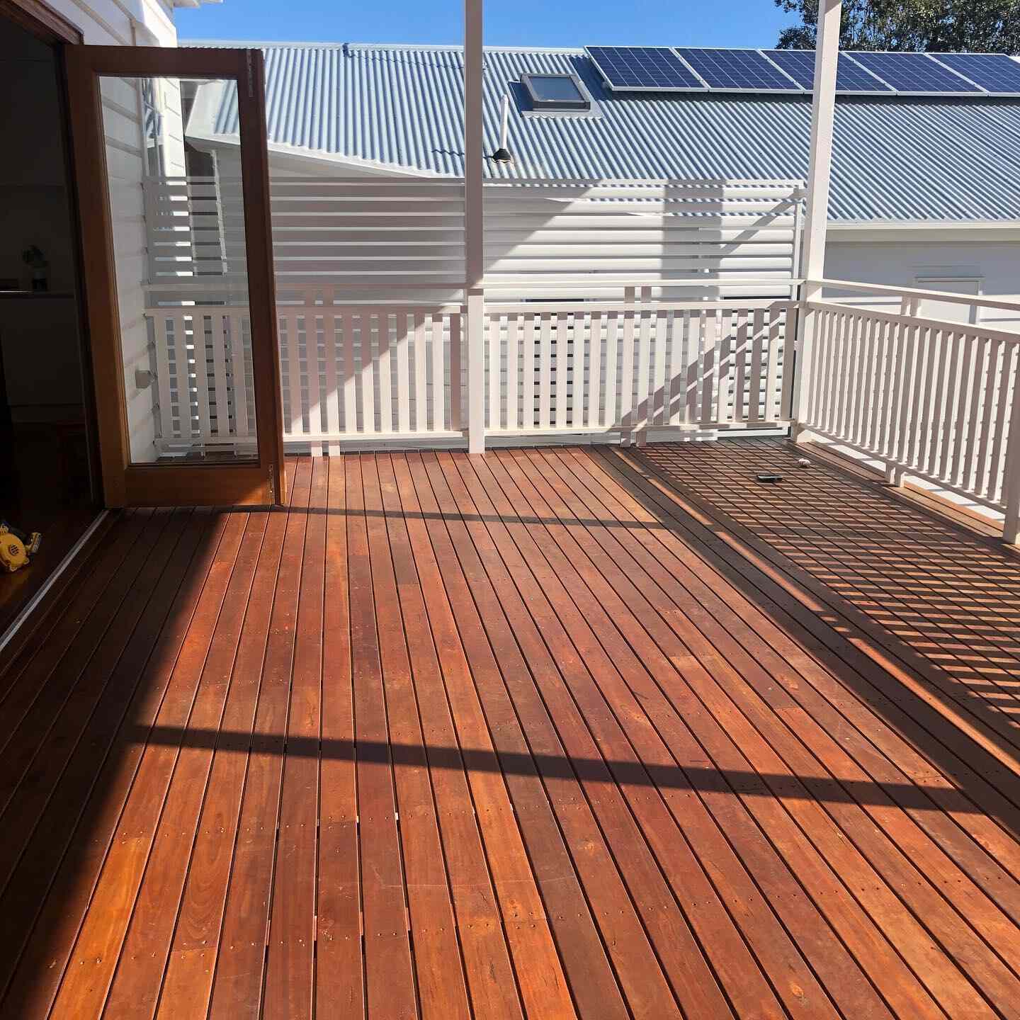 Oiled timber deck with white balustrade and an open timber door