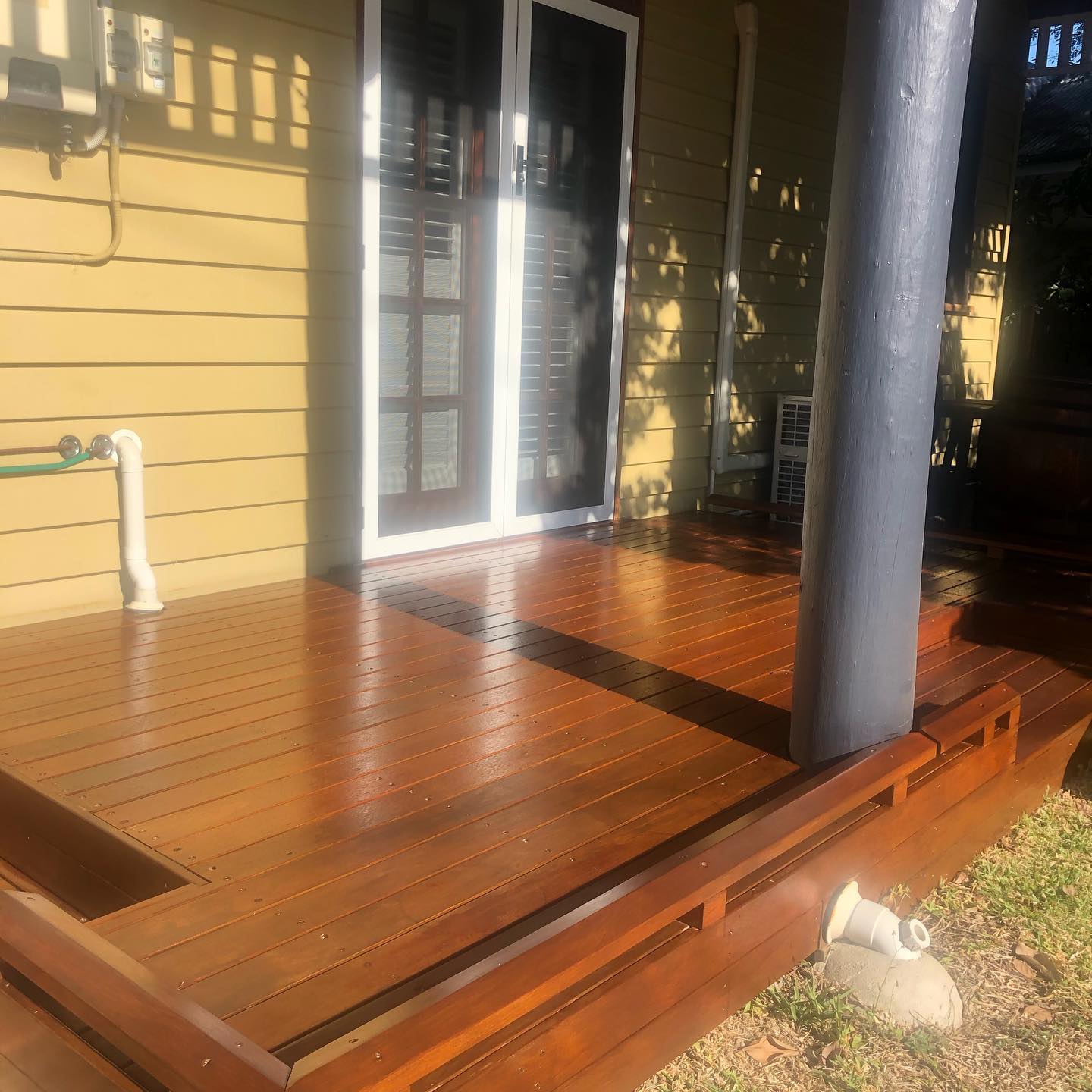 Oiled timber deck with a step around a dark post beside a cream house