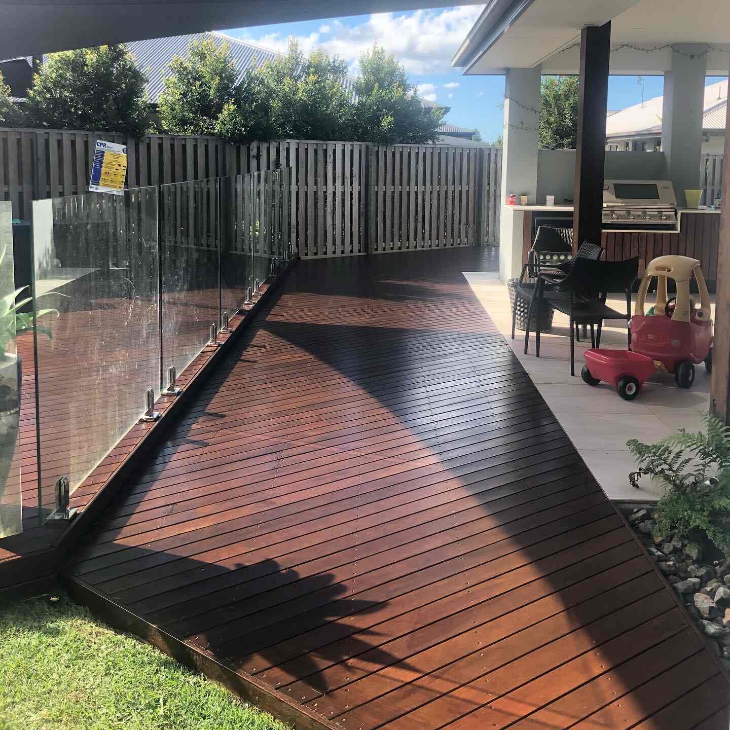 Oiled timber deck path along glass pool fencing to an outdoor kitchen
