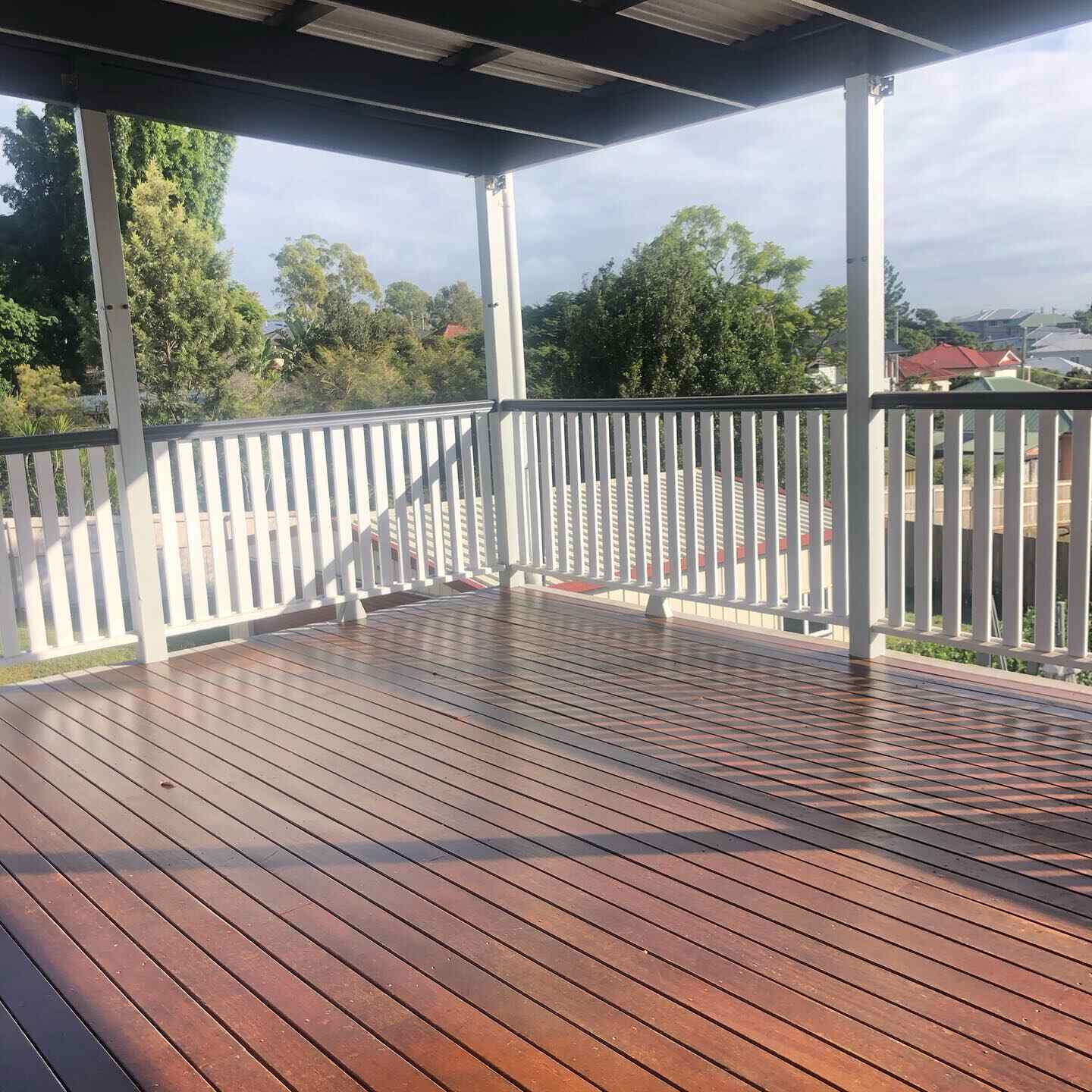 Oiled timber deck with white balustrade under a roof, overlooking trees
