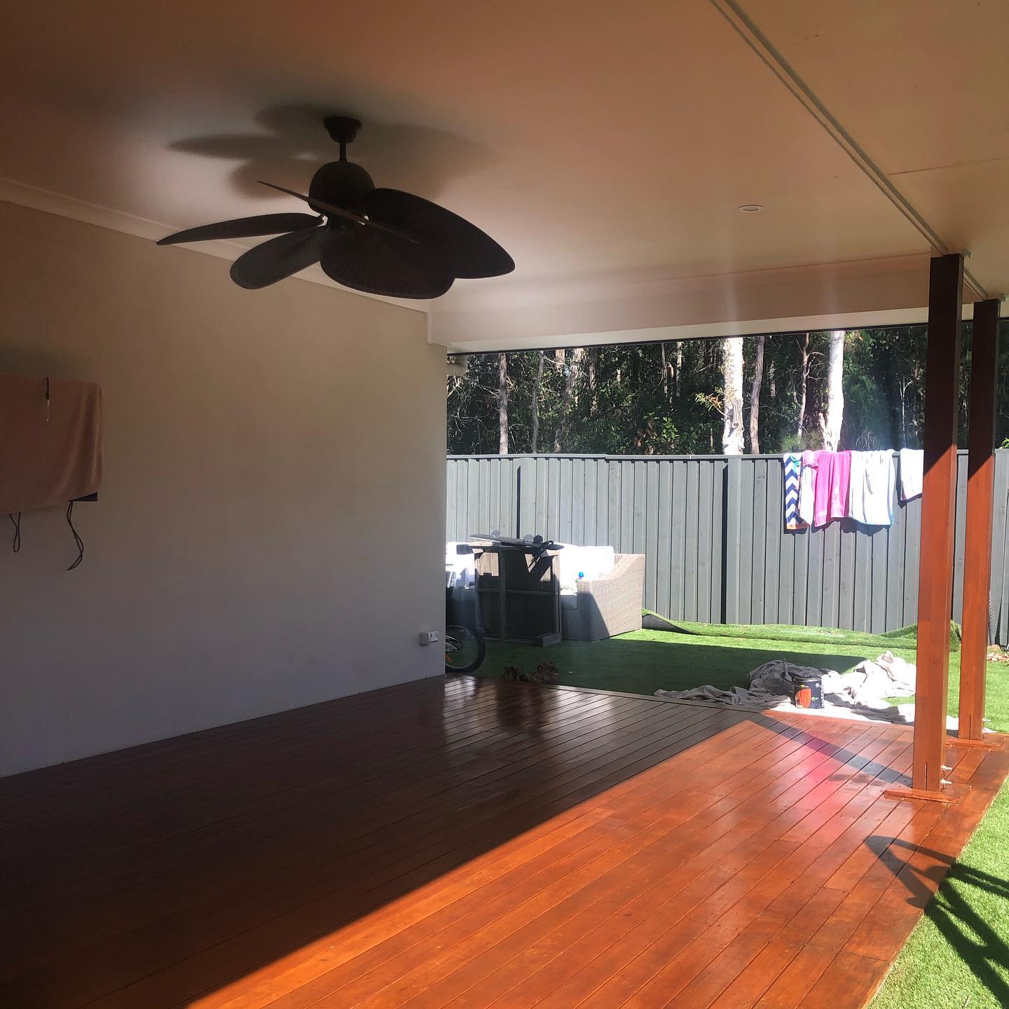 Oiled timber deck under a patio with a ceiling fan beside artificial turf