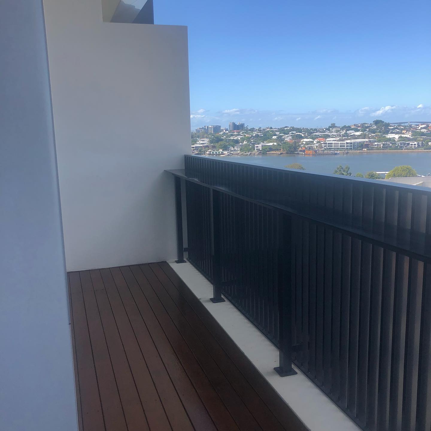 Narrow oiled timber balcony with black balustrade overlooking a river