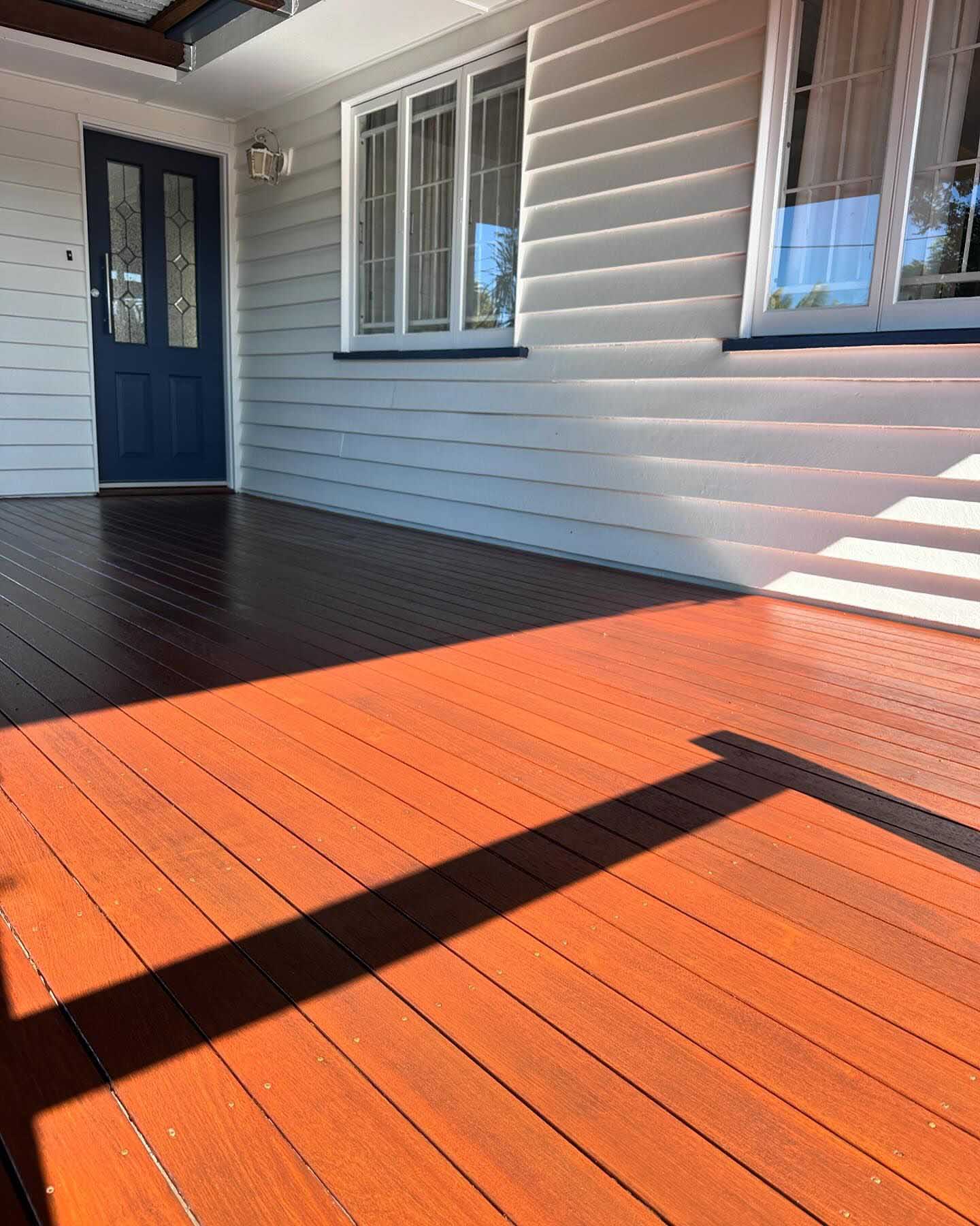 Freshly oiled timber verandah at the front of a weatherboard house with a navy door