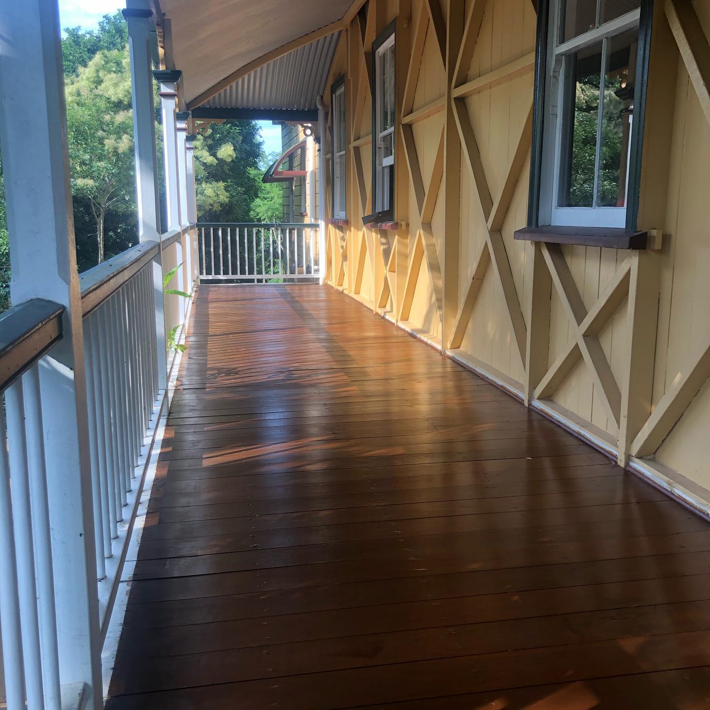 Glossy oiled timber verandah with white balustrade beside a cream cross-braced wall