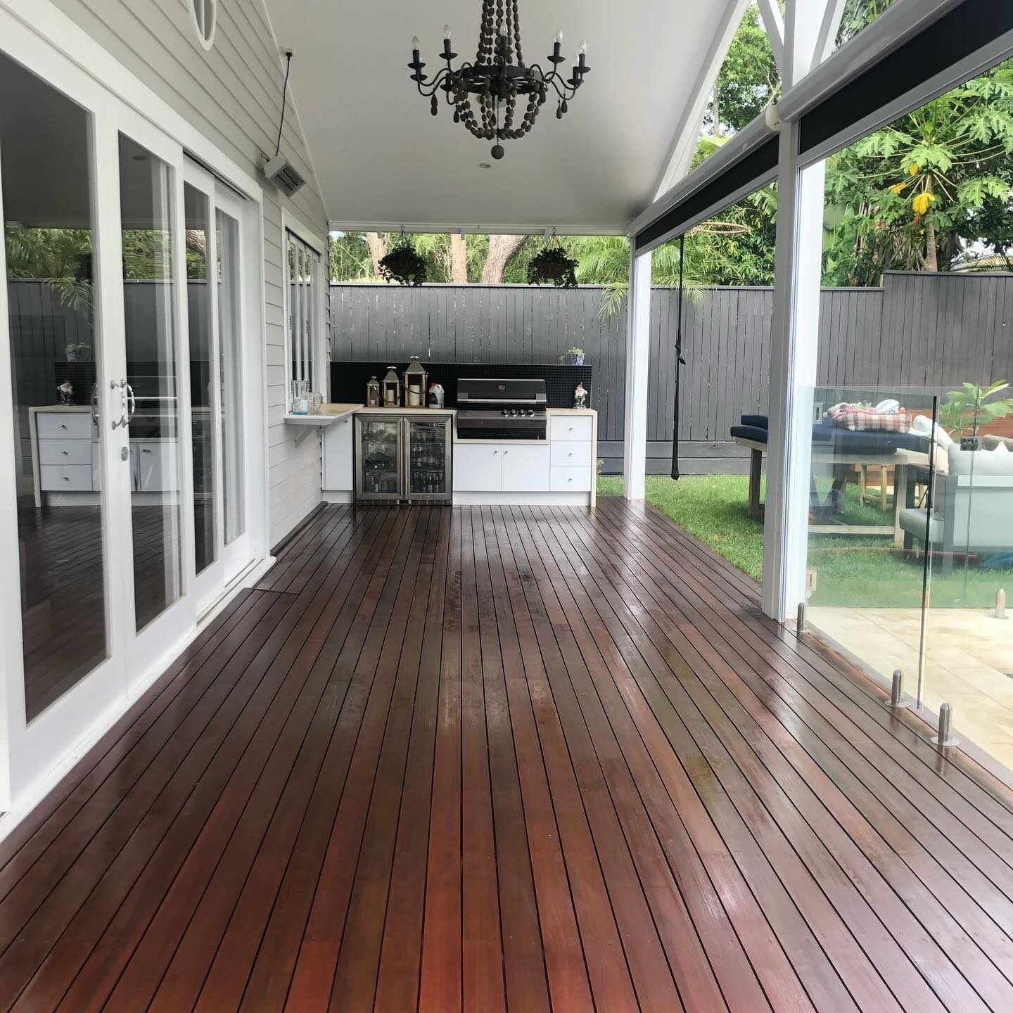 Oiled timber deck with glass fencing beside an outdoor kitchen and chandelier