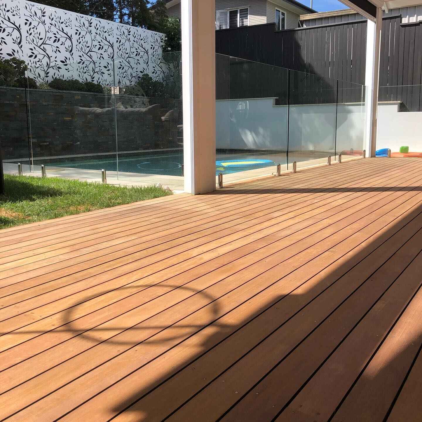 Freshly oiled pale timber deck with glass pool fencing and a decorative screen