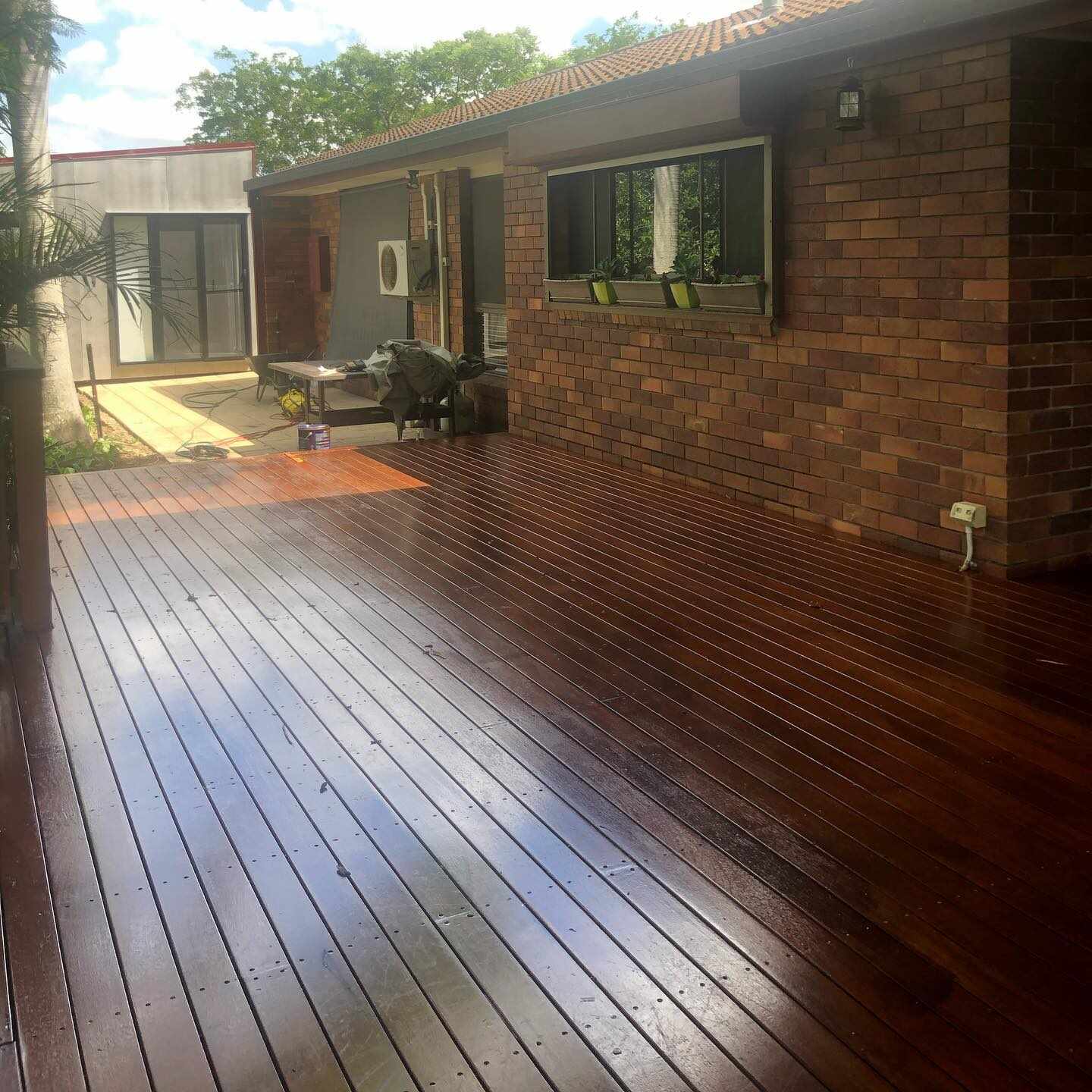 Glossy dark oiled timber deck beside a brick house