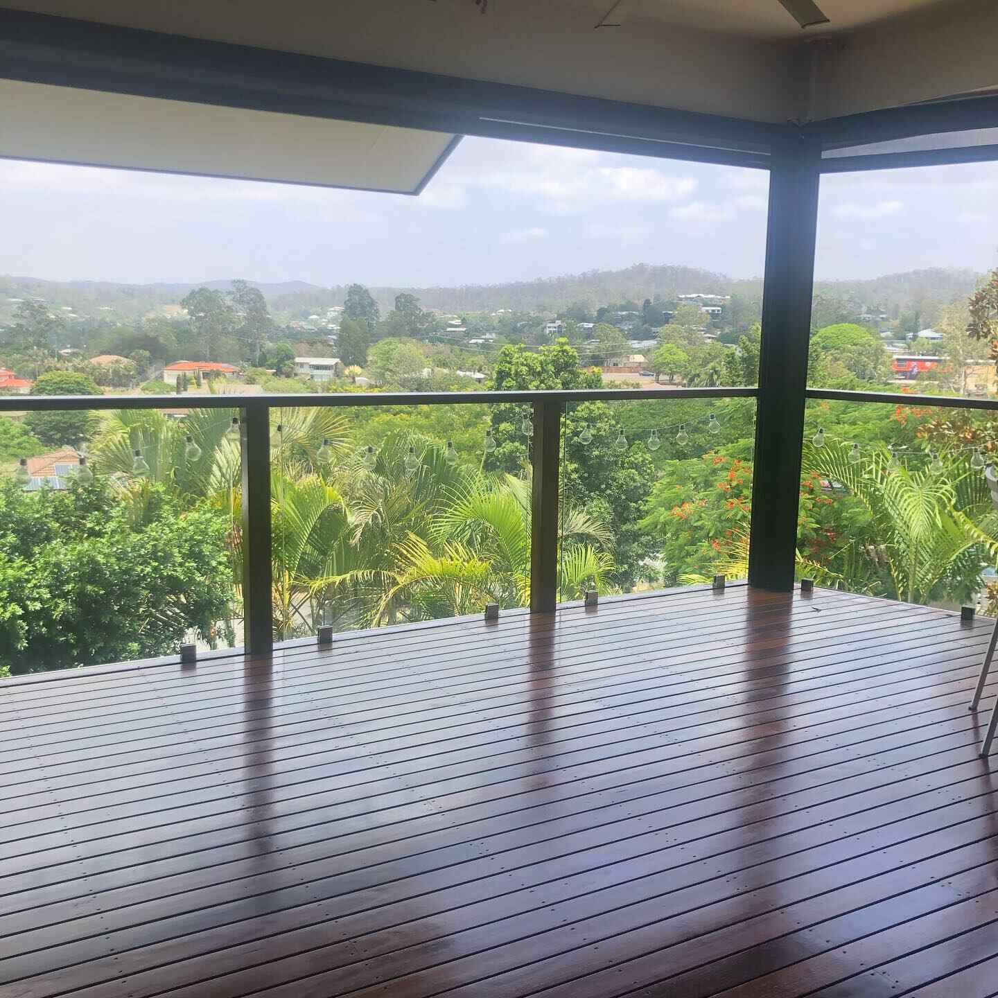 Glossy oiled timber deck with glass and timber balustrade overlooking suburbs