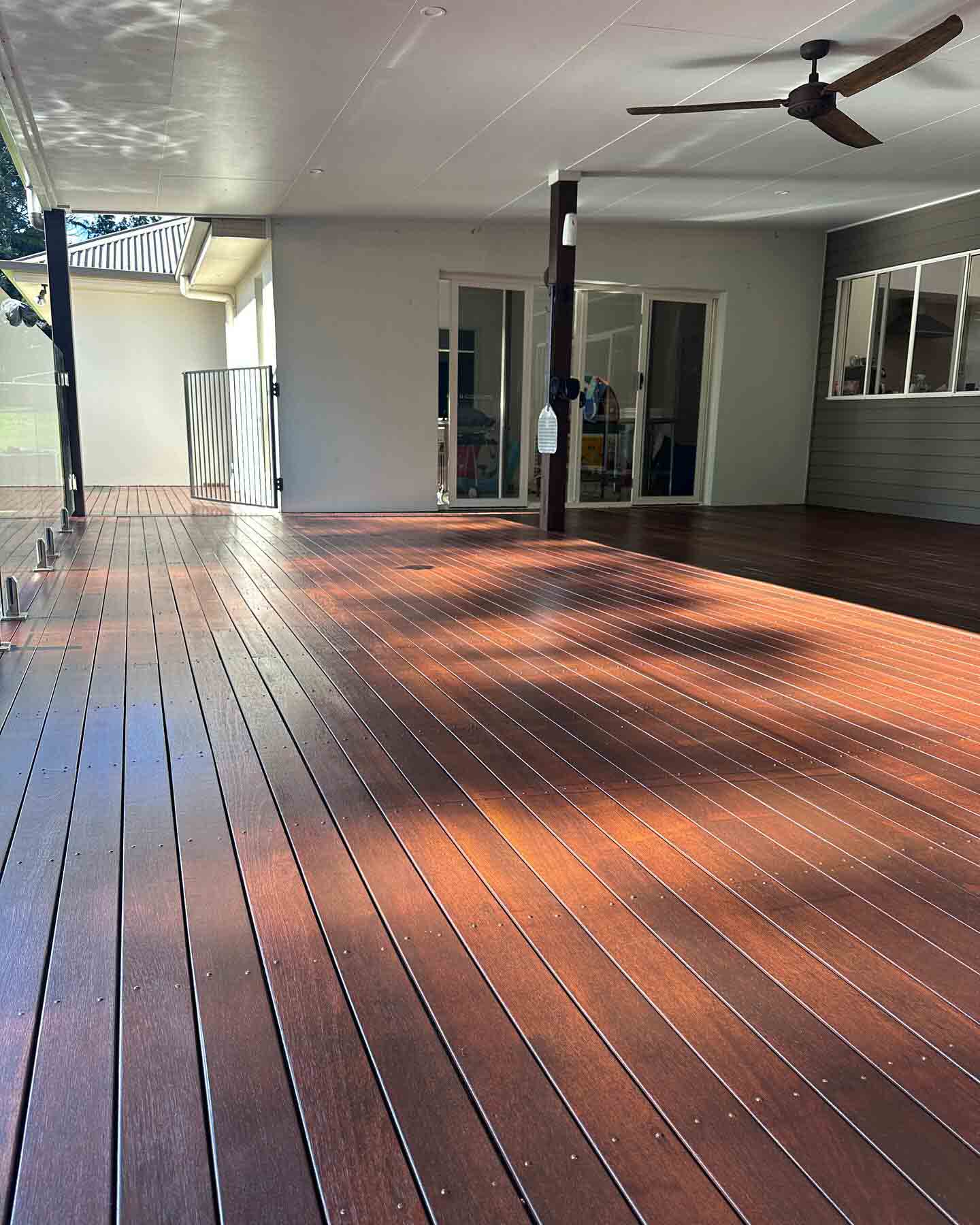Large covered timber deck in afternoon light outside a rendered house