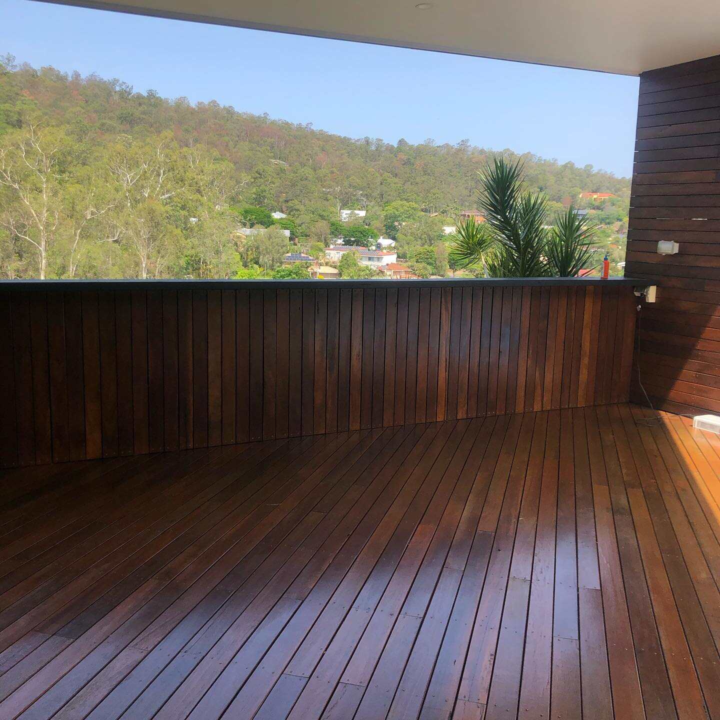 Glossy oiled timber deck with a solid timber balustrade wall overlooking a hill