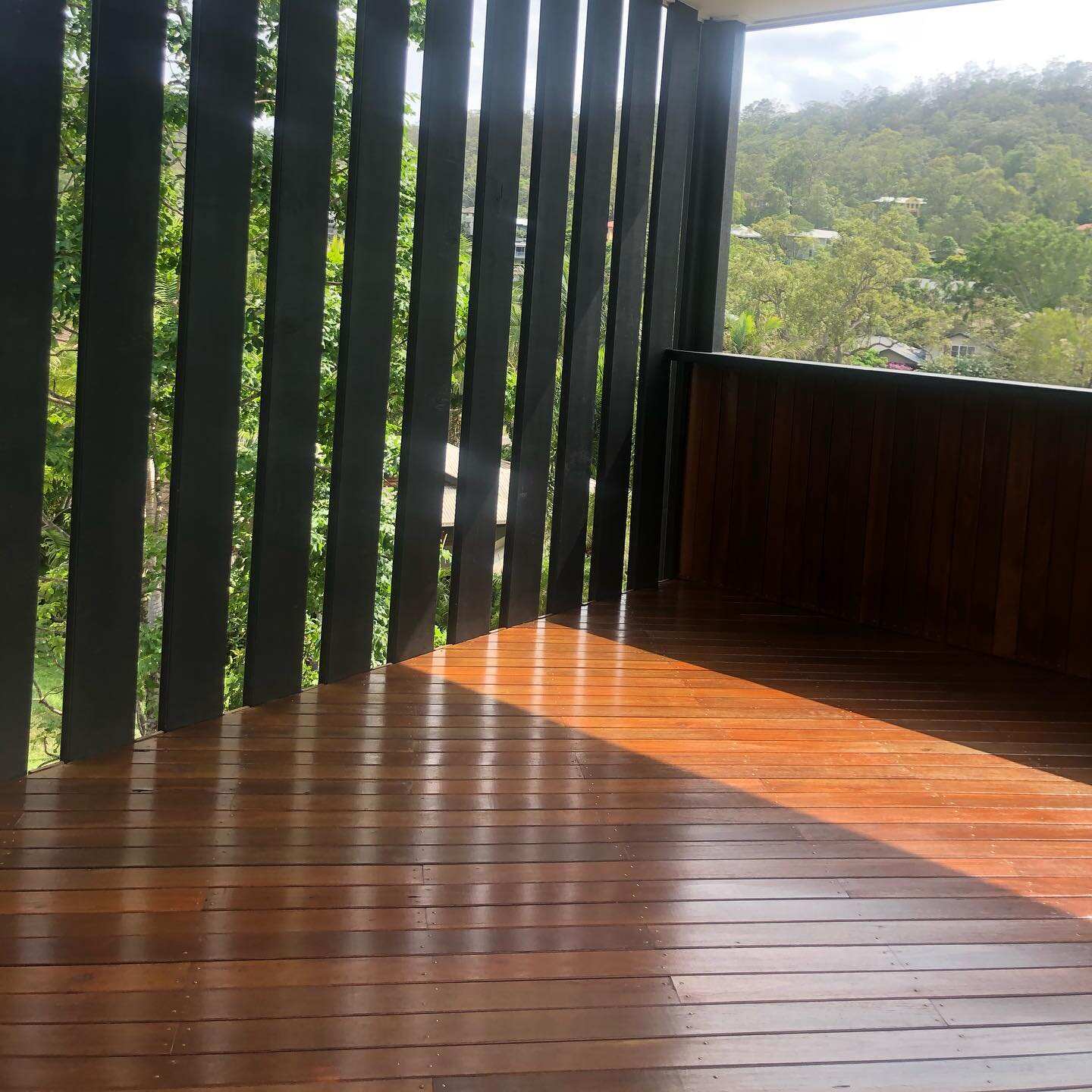 Glossy oiled timber deck with tall black vertical battens and a hillside view