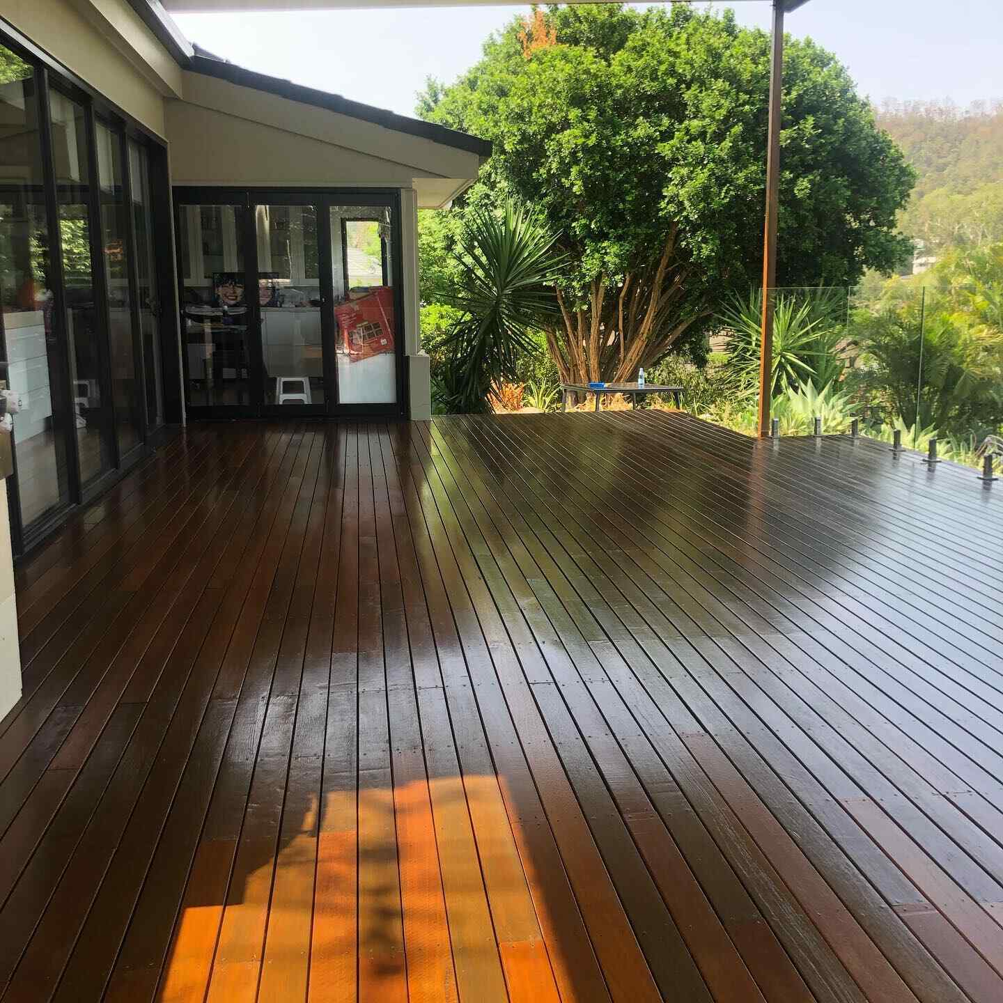Glossy oiled timber deck outside bi-fold doors with trees beyond