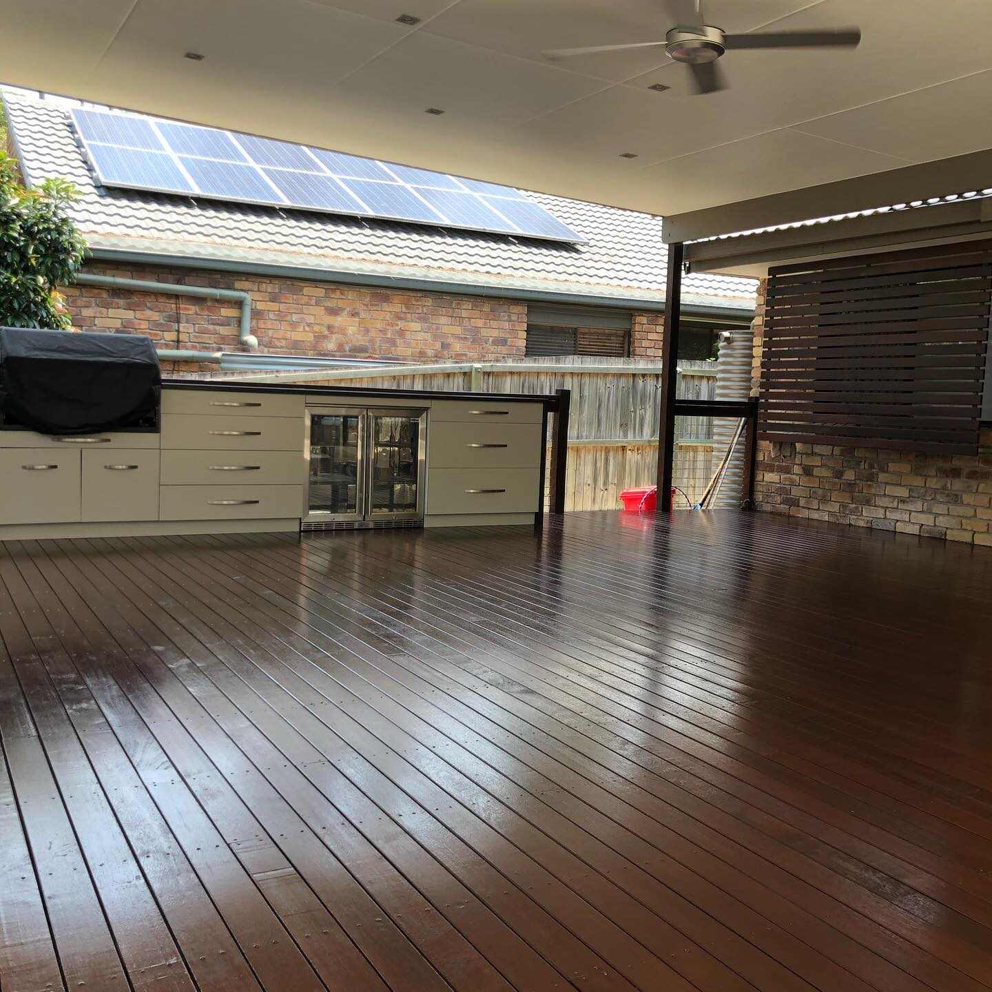 Glossy oiled timber deck under a patio roof with an outdoor kitchen