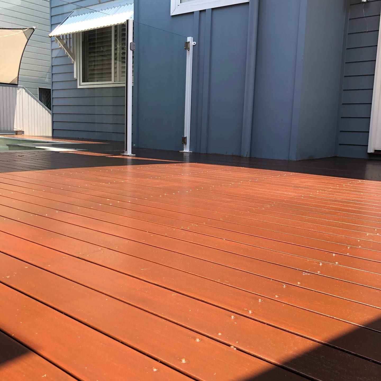 Freshly oiled red-toned deck beside a blue weatherboard house