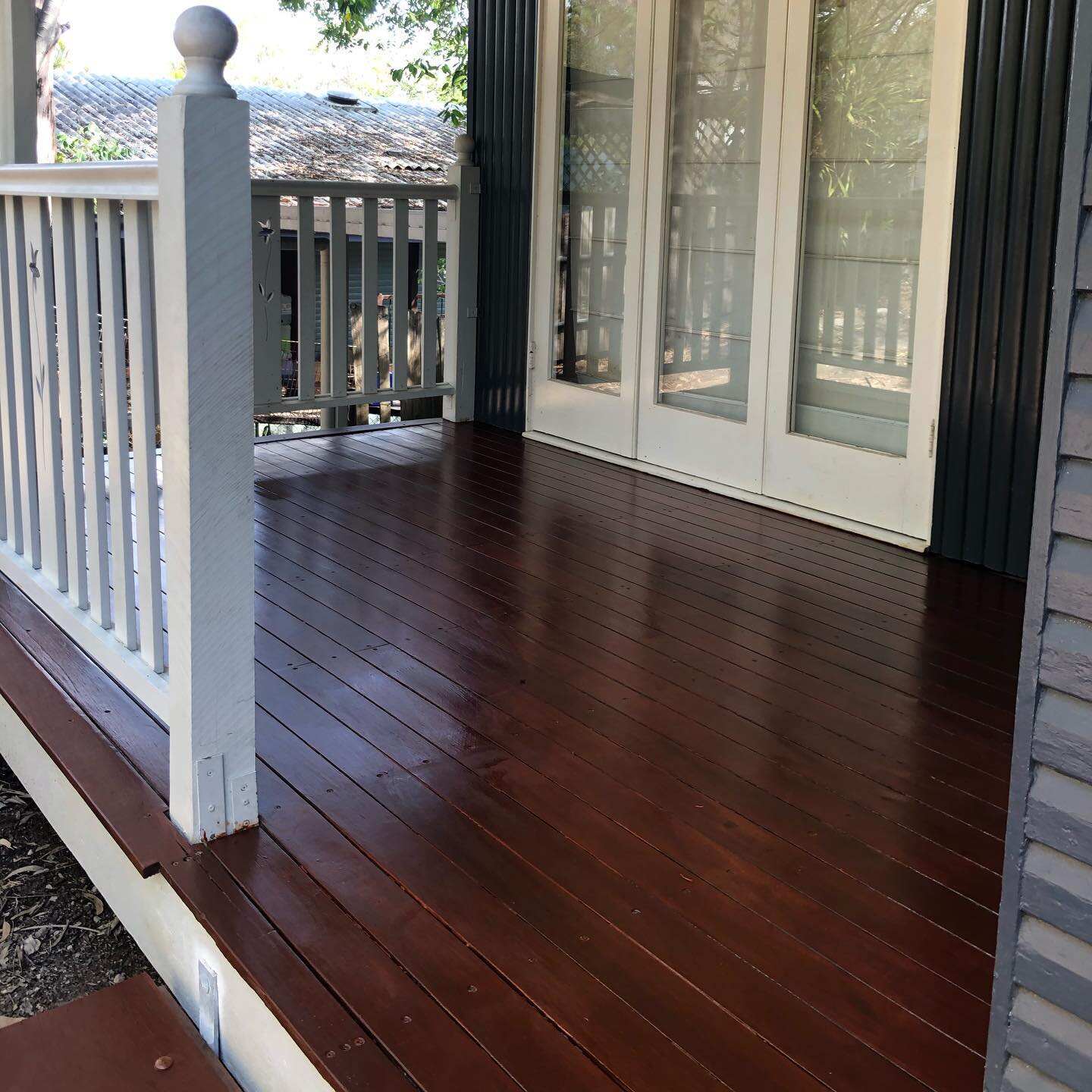 Dark oiled timber verandah outside white French doors with white balustrade