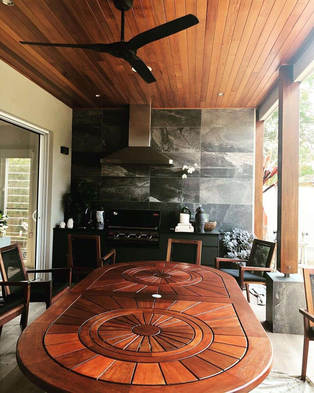 Covered outdoor room with a timber-lined ceiling, round timber table and outdoor kitchen