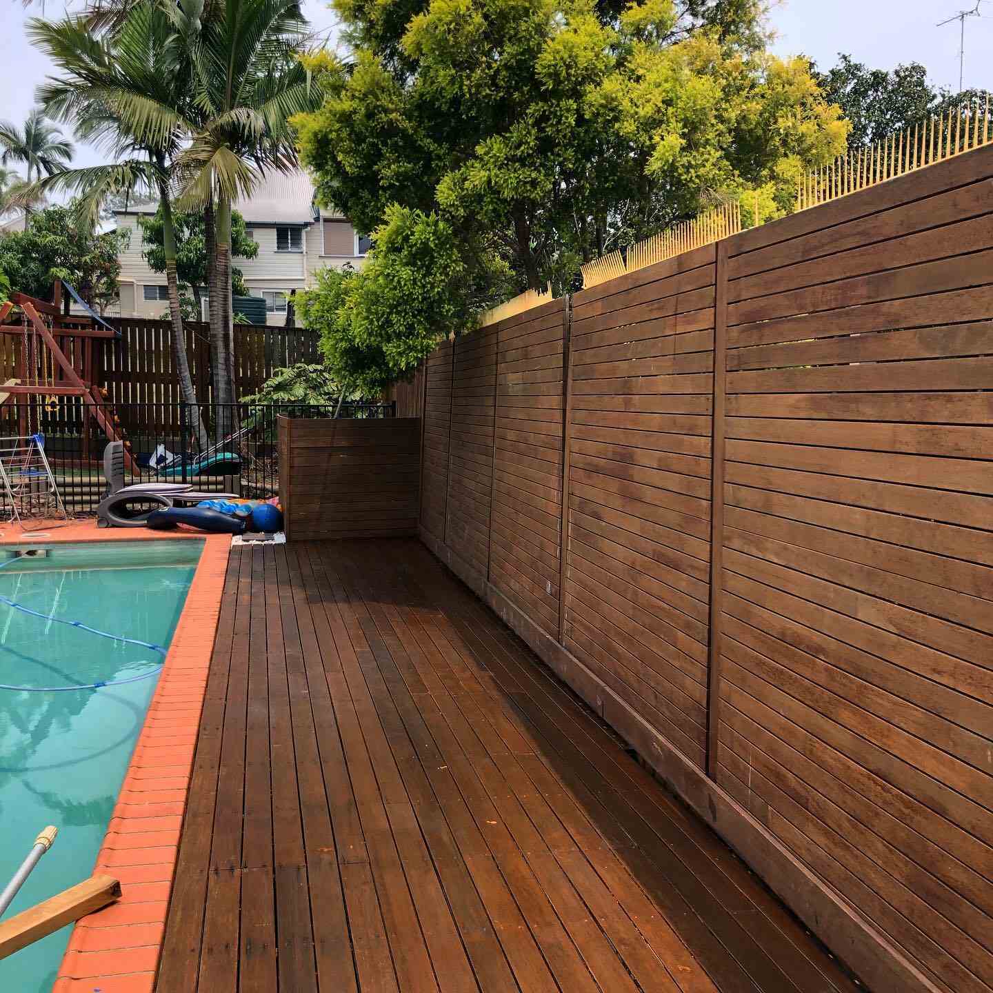Oiled timber deck along a pool with a horizontal timber slat fence