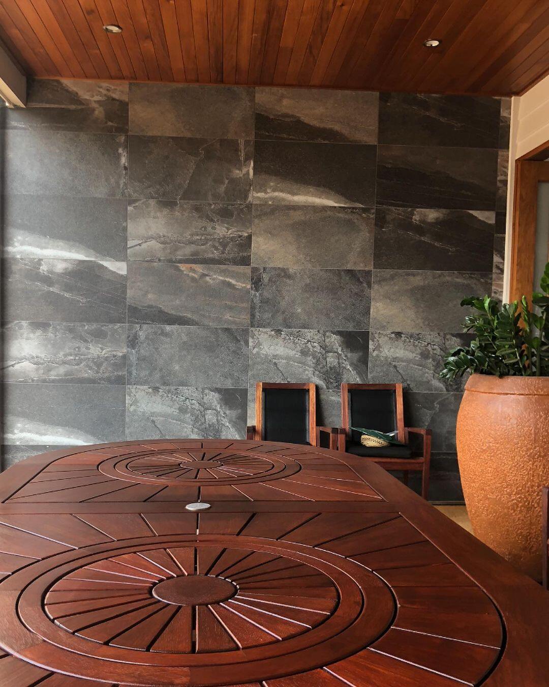 Round timber outdoor table under a timber-lined ceiling beside a stone-tiled wall