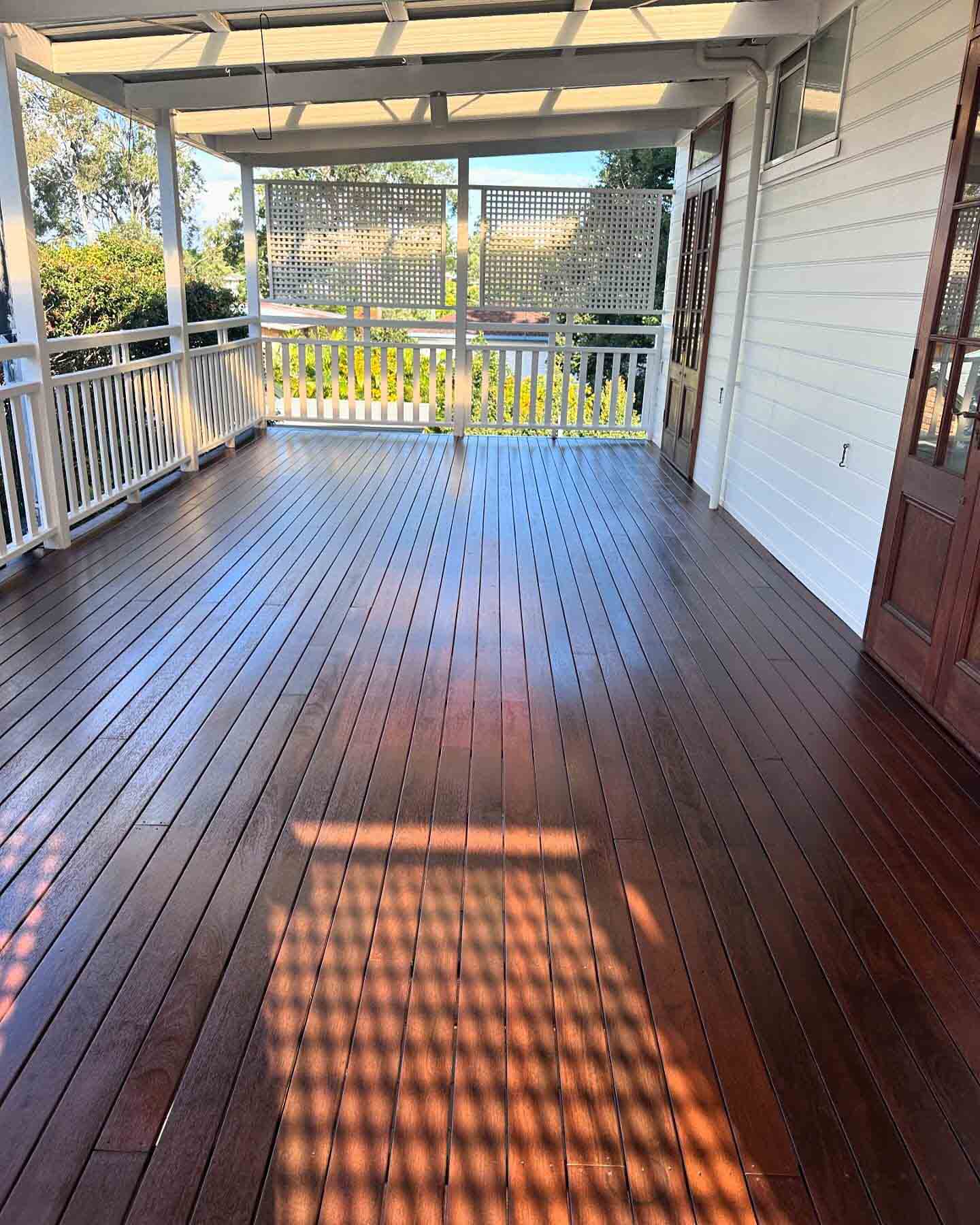 Dark oiled timber verandah with white balustrade and sunlight through lattice