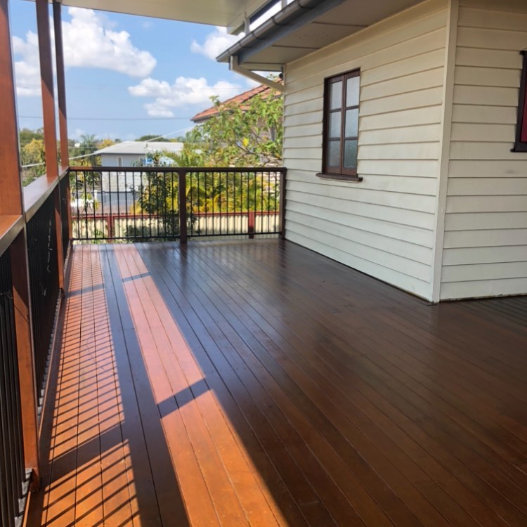 Oiled timber verandah with timber and black balustrade beside a weatherboard house