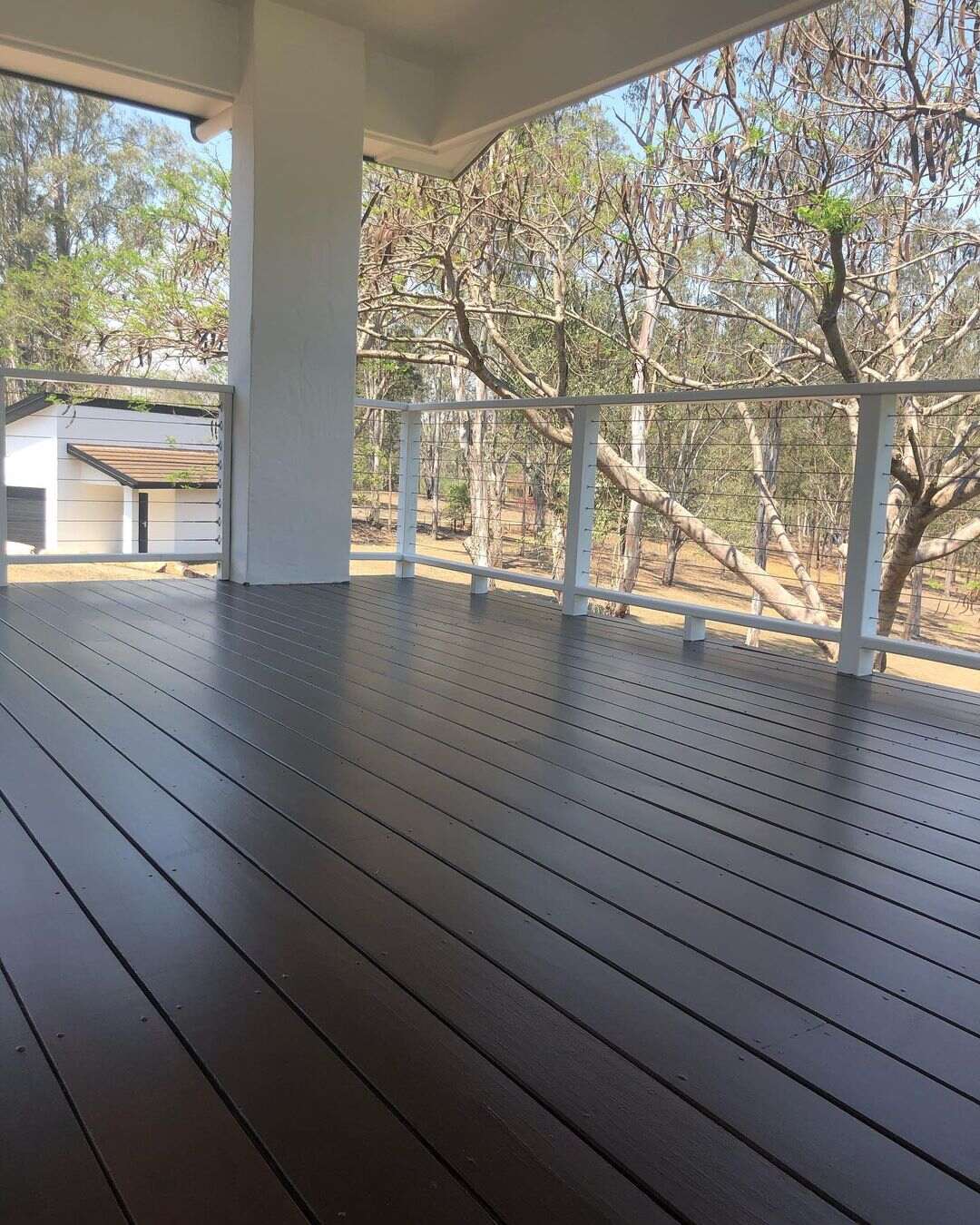 Dark oiled timber deck with white balustrade overlooking gum trees