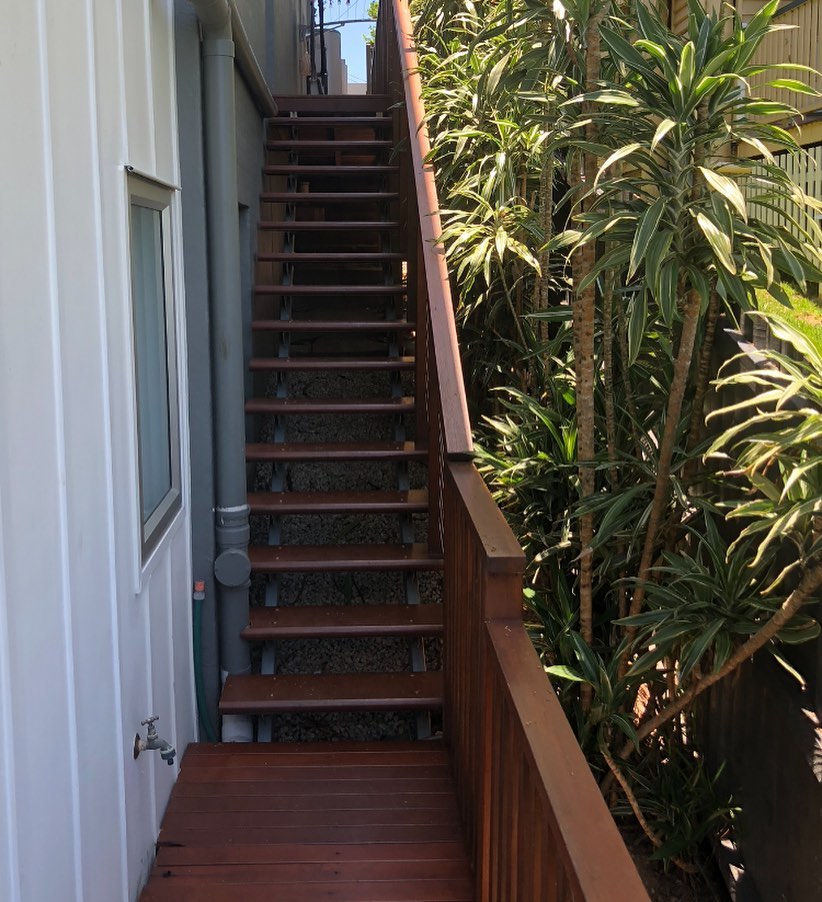 Oiled timber stairs and landing with timber balustrade beside a white house