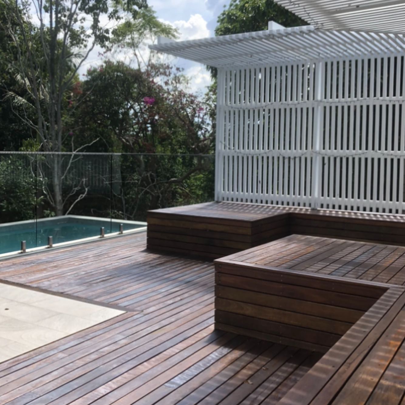 Oiled timber pool deck with built-in timber bench seats and a white slatted screen