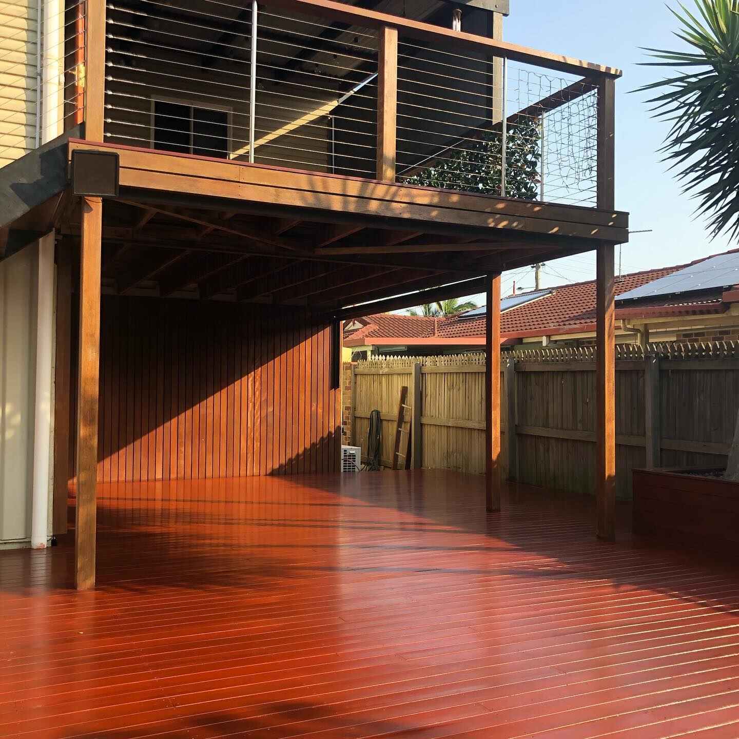 Glossy red-toned timber deck under a timber balcony with wire balustrade