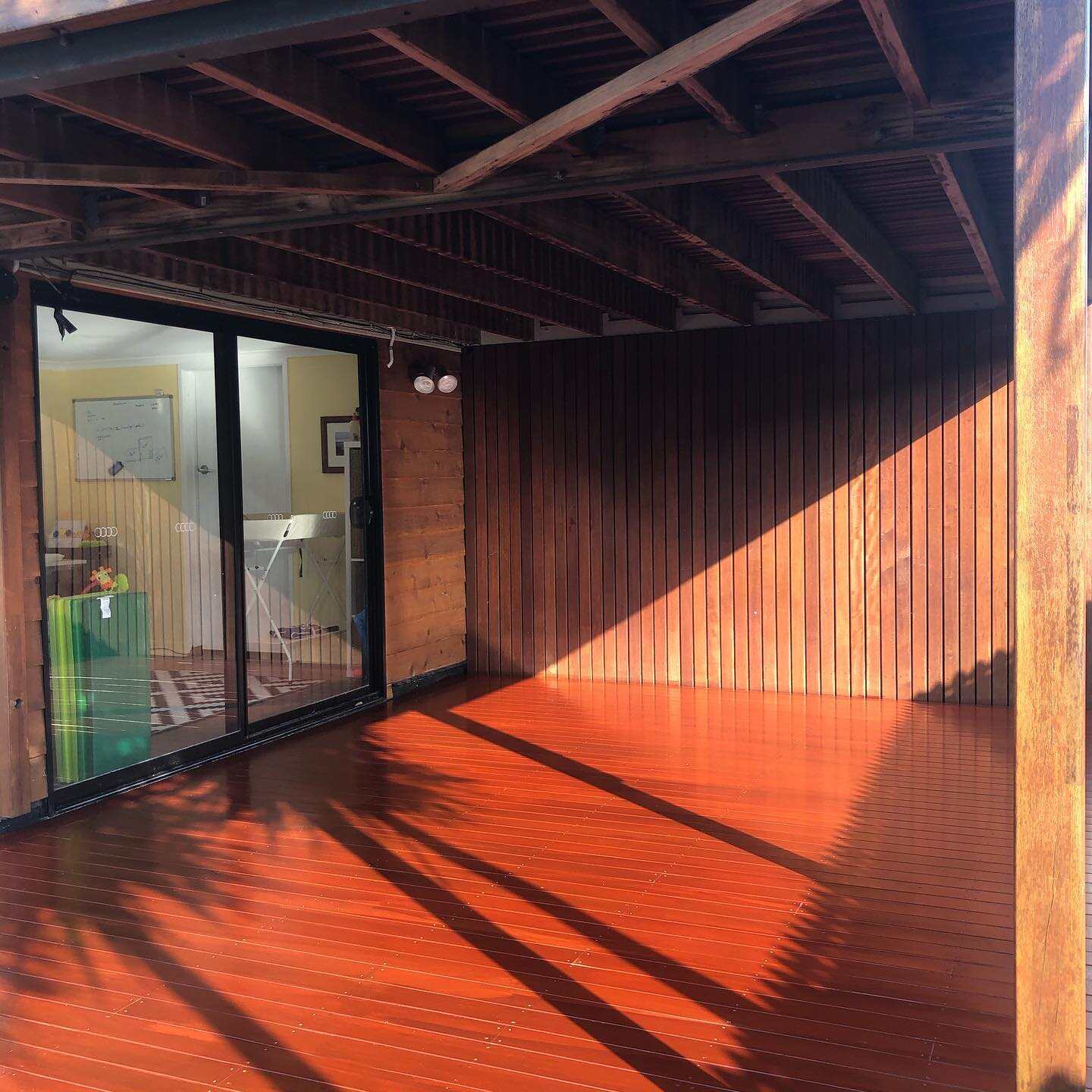 Glossy red-toned timber deck under exposed rafters with timber-clad wall