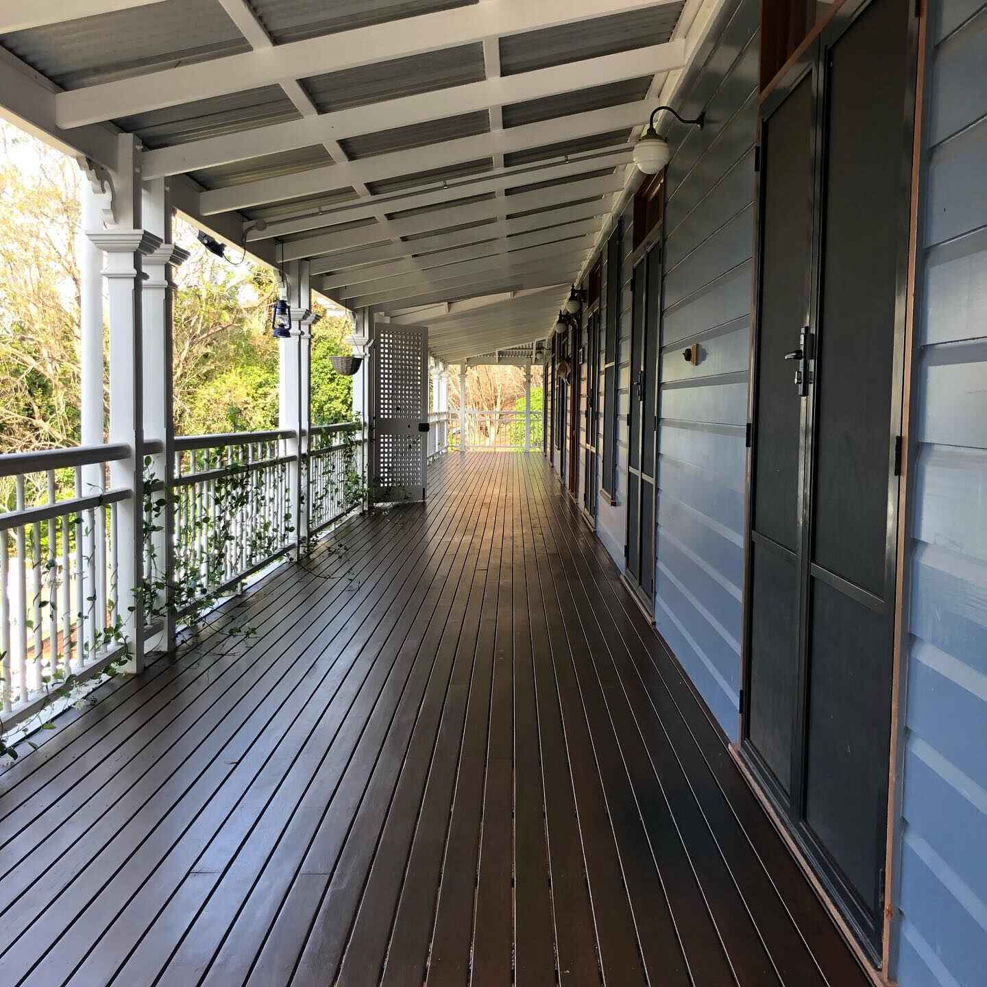 Long dark oiled timber verandah with white lace balustrade along a grey house