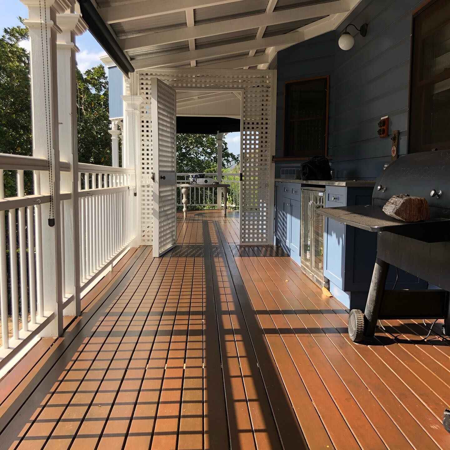 Oiled timber verandah with white balustrade and lattice beside an outdoor kitchen