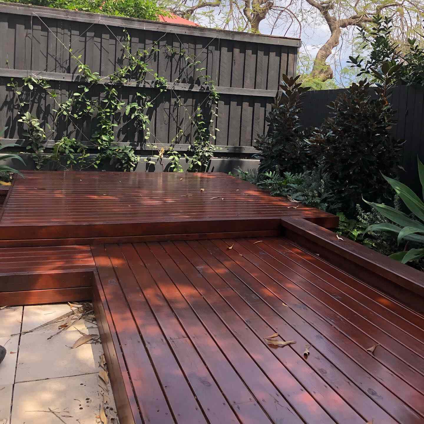 Two-level oiled timber garden deck beside a dark slatted fence