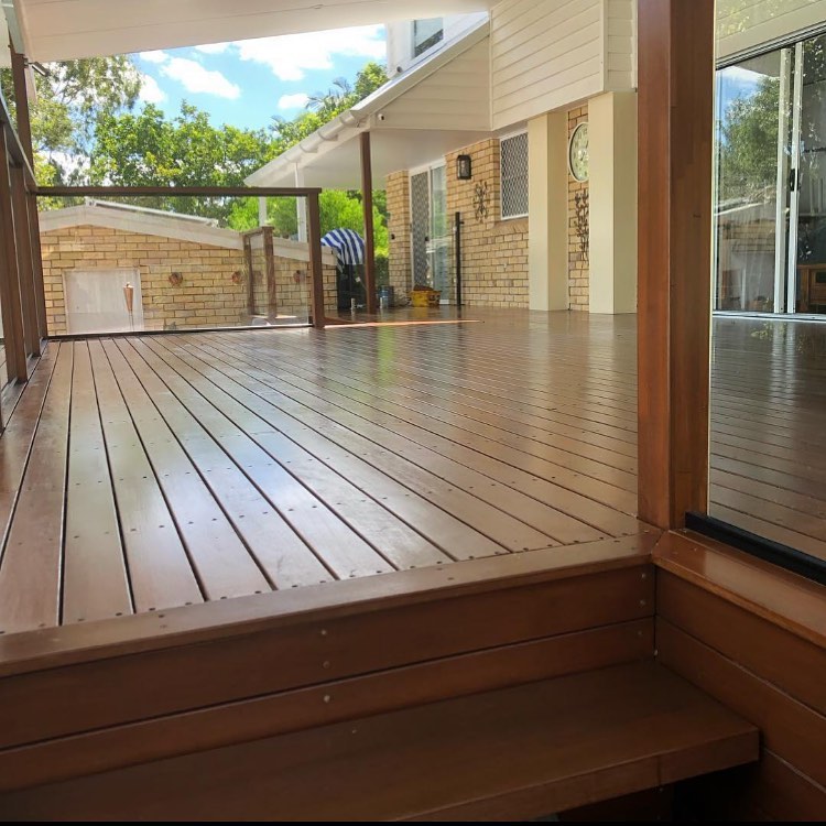 Oiled timber deck with a step down, beside glass doors and a brick house