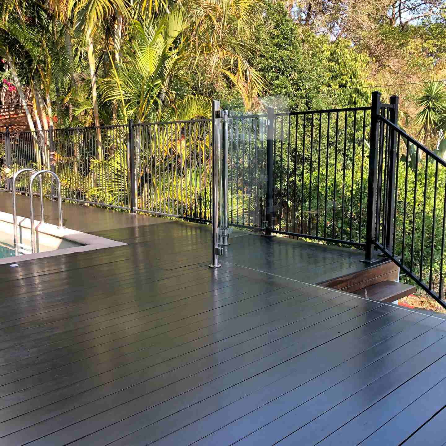 Dark-coated pool deck with black pool fencing and palms