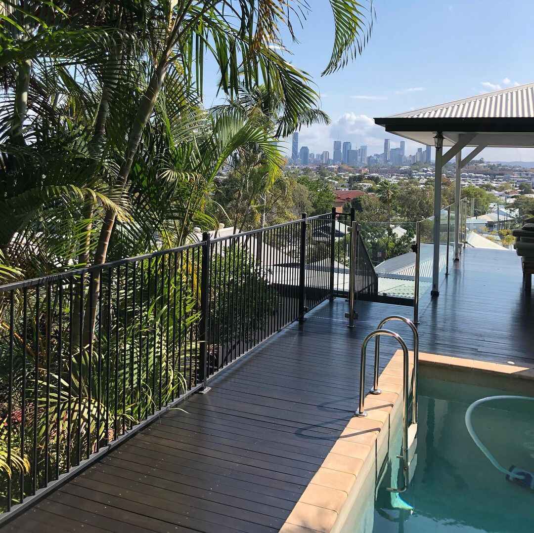 Dark-coated deck beside a pool with black fencing and a city view