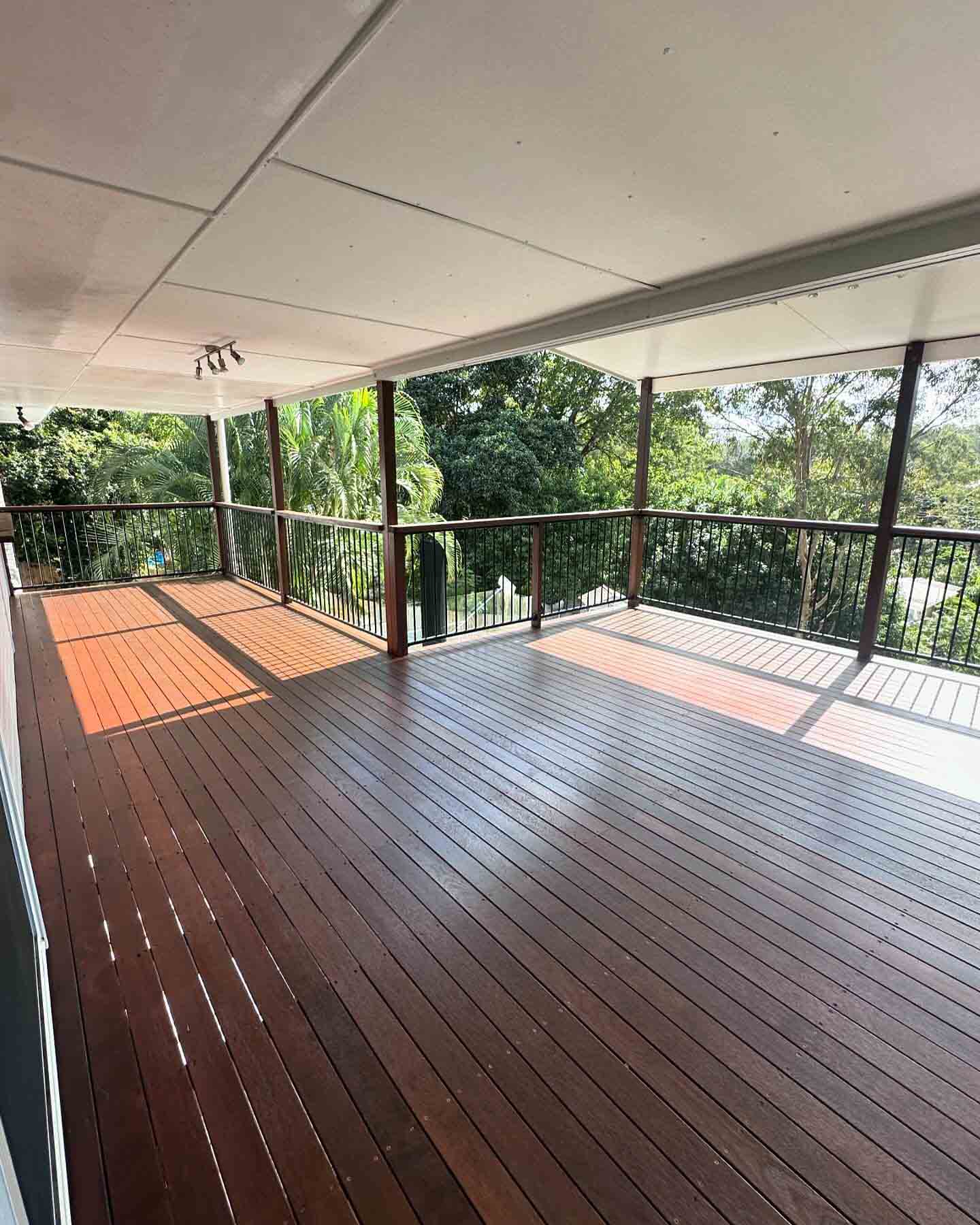 Dark oiled timber deck under a white roof with black metal balustrade overlooking trees