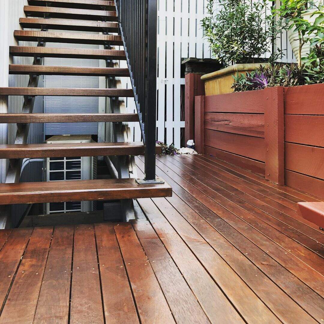 Oiled timber deck at the foot of open timber stairs beside a timber planter