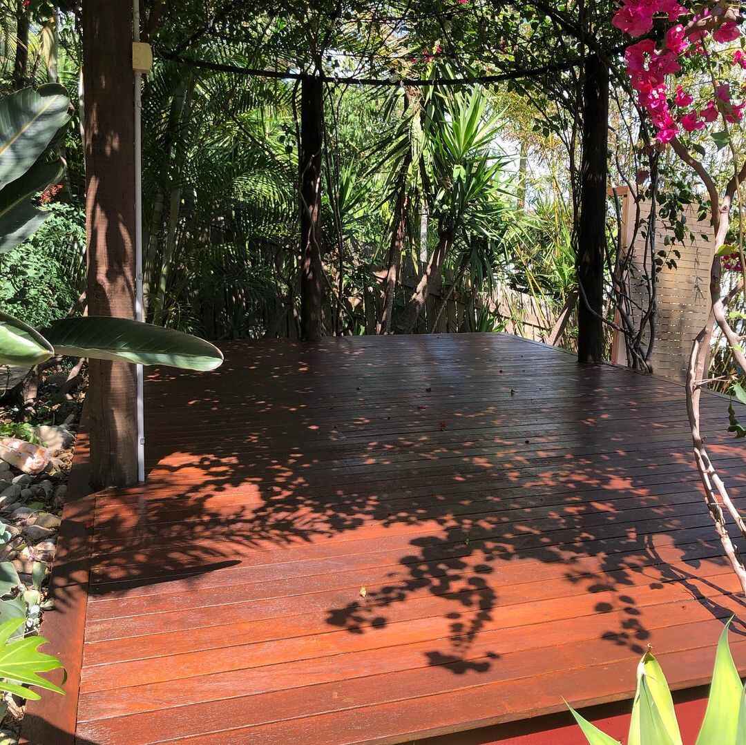 Oiled timber garden deck under a tree with dappled shade