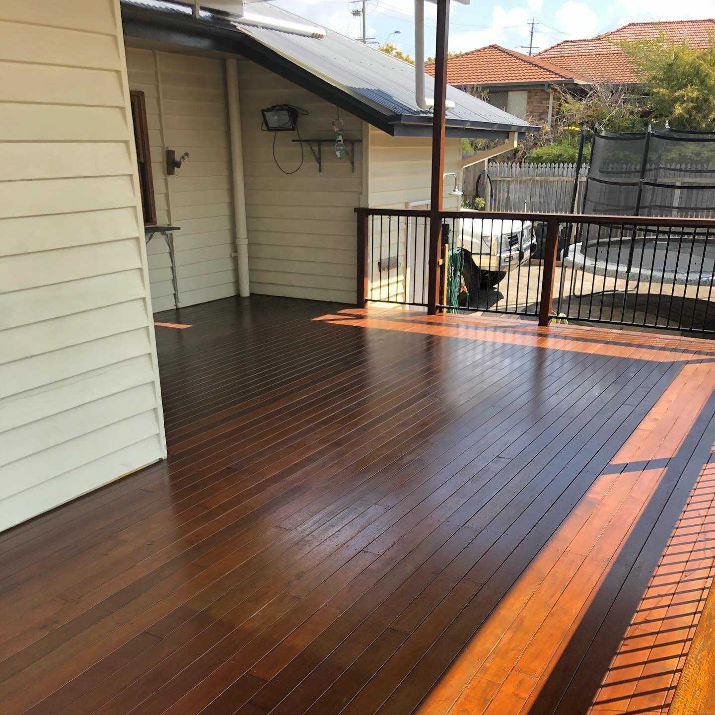 Oiled timber deck with dark timber balustrade beside a cream weatherboard house