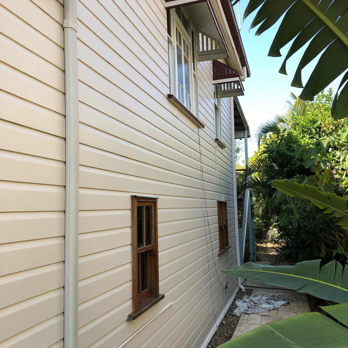 Cream weatherboard wall with timber-framed windows beside a garden path
