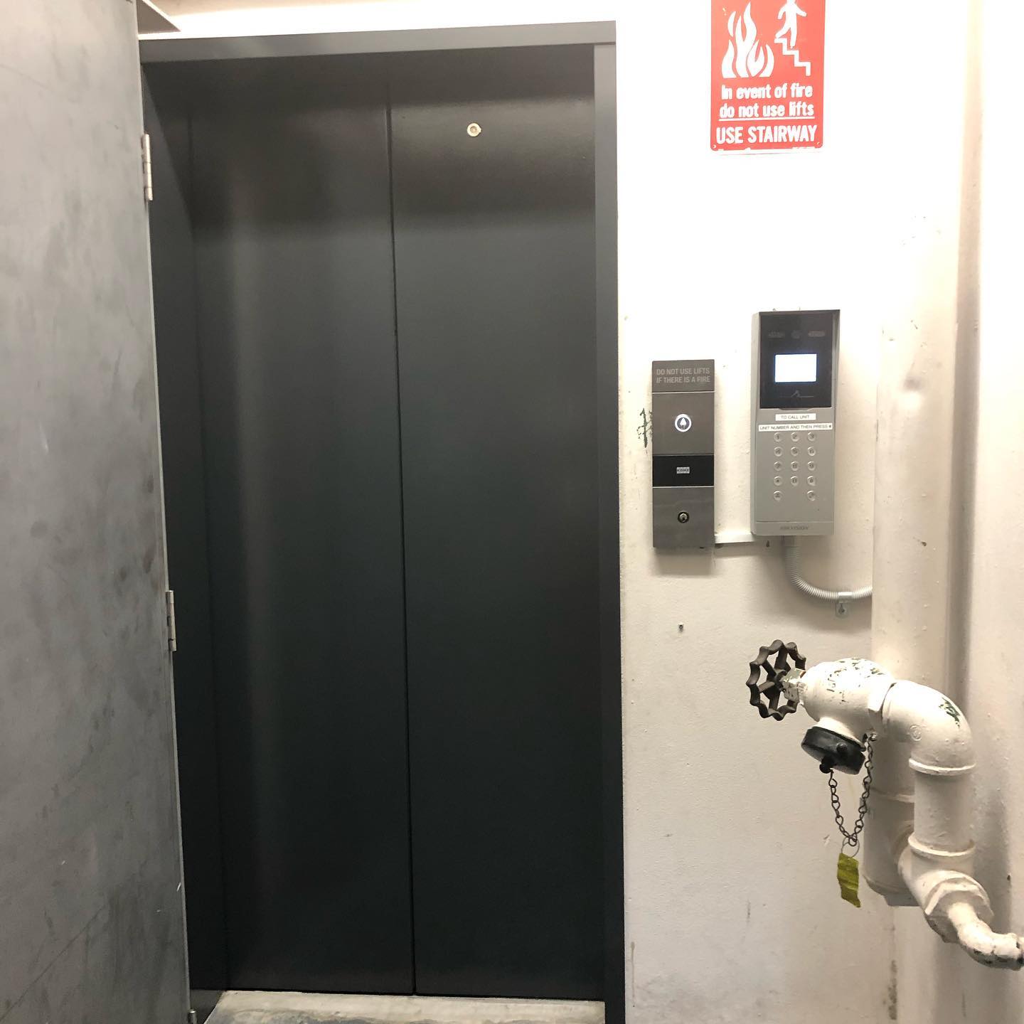 Dark grey lift door beside an intercom panel in a building foyer